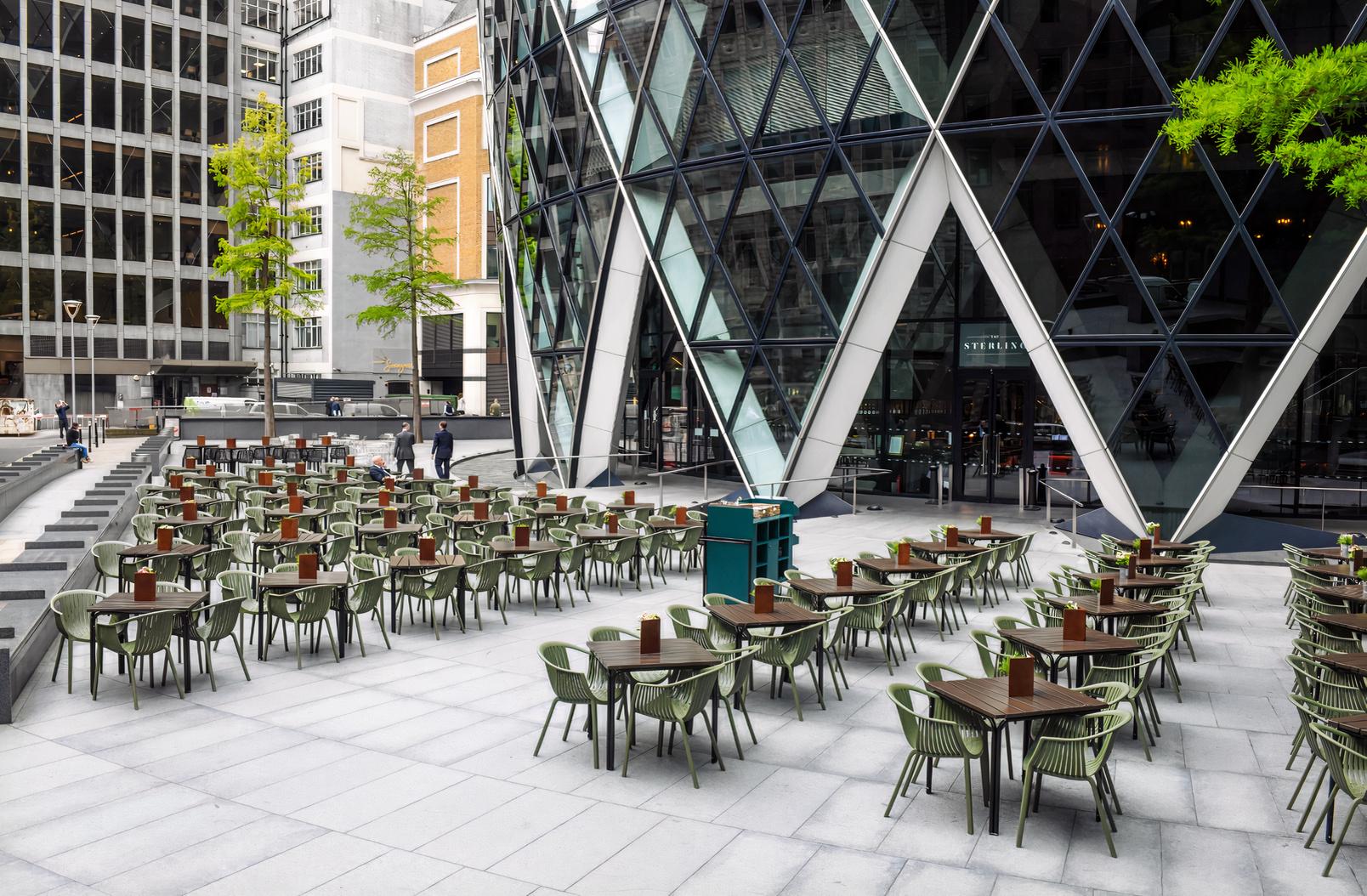 An outdoor pub area with rows of green chairs and wooden tables on a paved terrace at The Sterling.