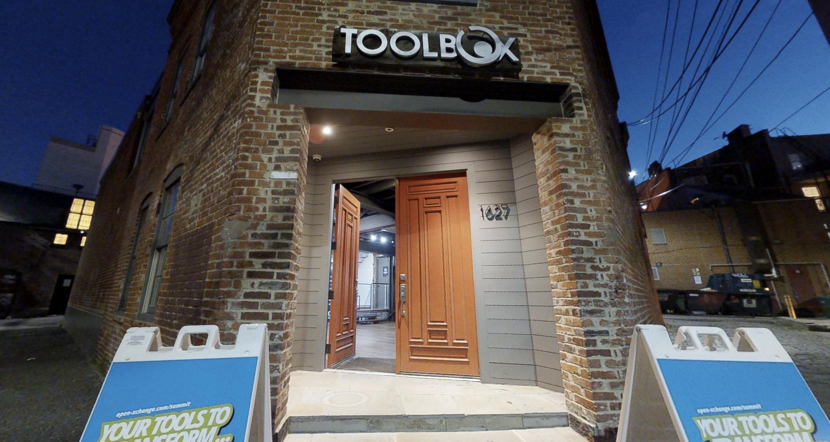 A gallery with a brick exterior facade and wide wooden double doors at Toolbox Art Studio.