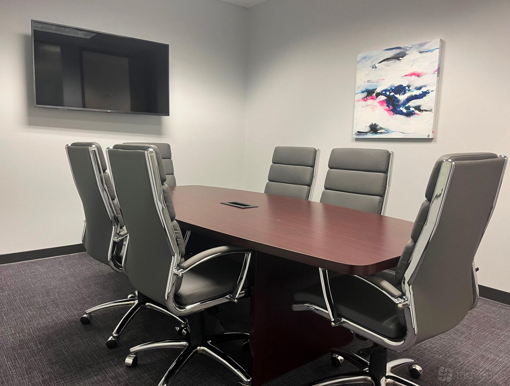 A meeting room with a dark wood conference table, gray executive chairs, wall-mounted TV, and abstract artwork at Peachtree Offices Dunwoody.
