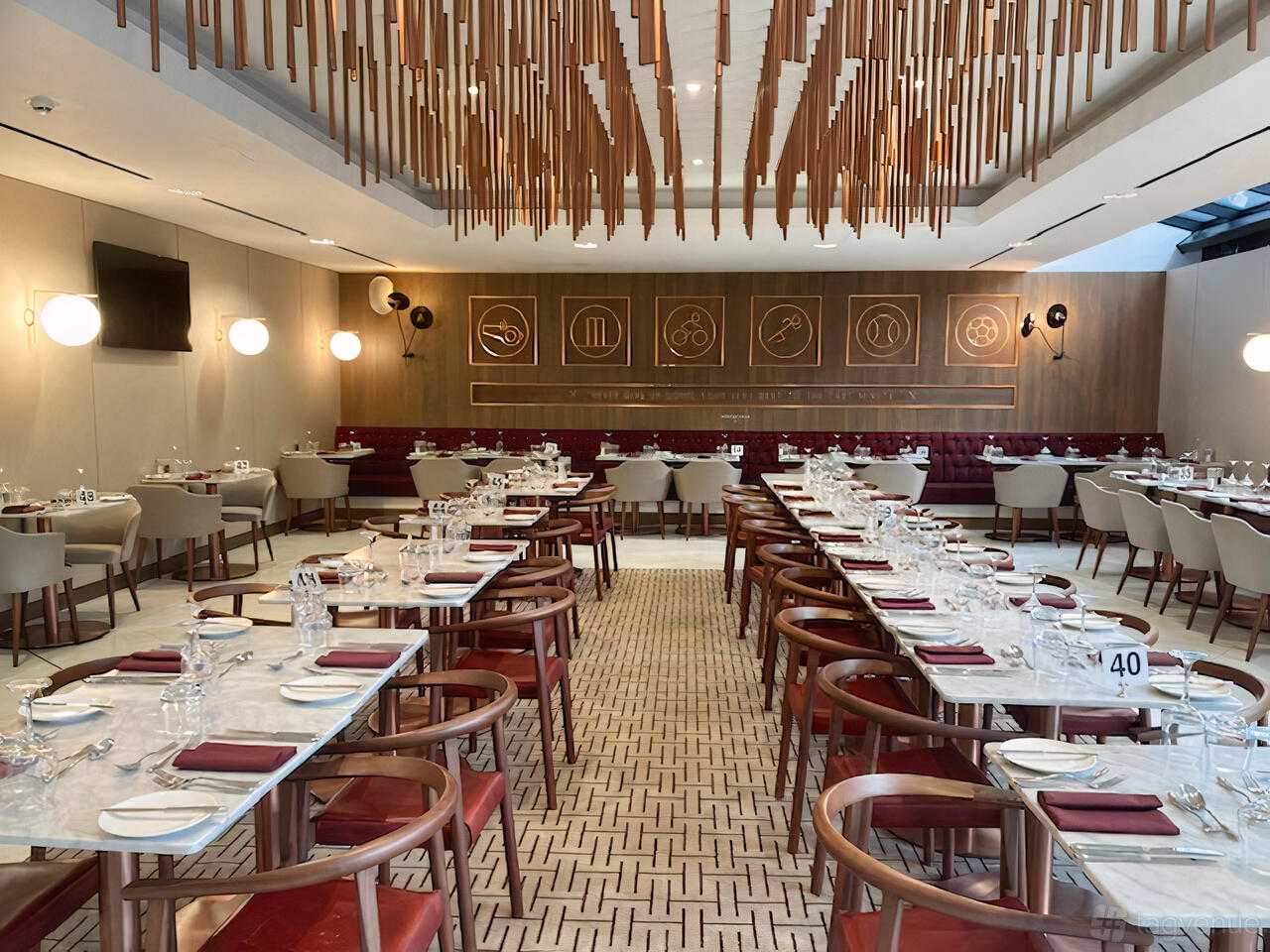 An event space with marble-top tables, wooden chairs, and sculptural ceiling decor at London Stadium's The Arnold Hills.