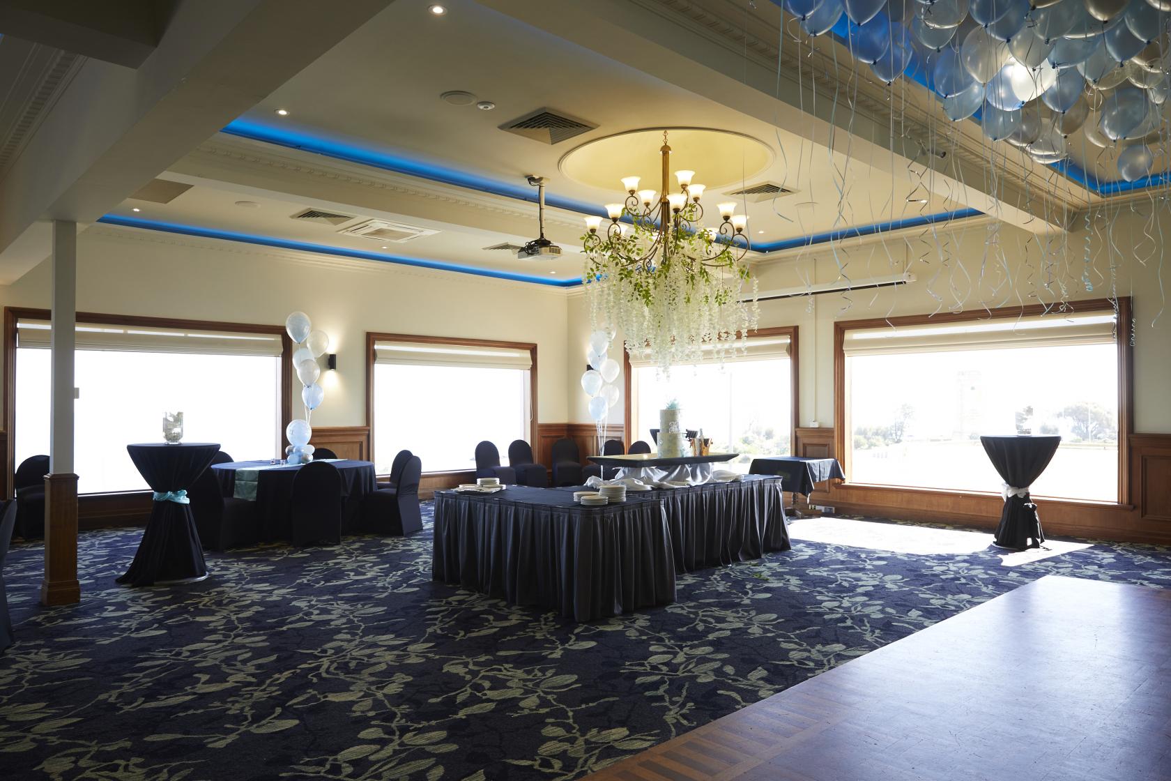 A pub event room with large windows, blue patterned carpet, and tables draped in black linens at Brighton Beach Hotel.