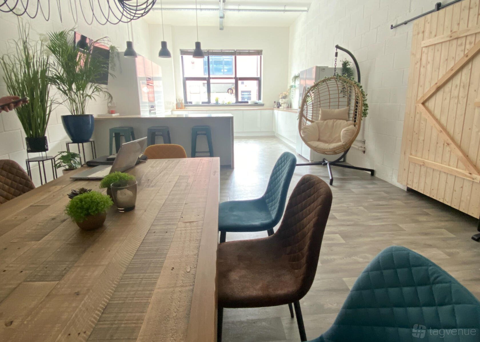 A meeting room with a wooden table, colorful chairs, hanging lights, and a swing chair at Xenia Philosophy.
