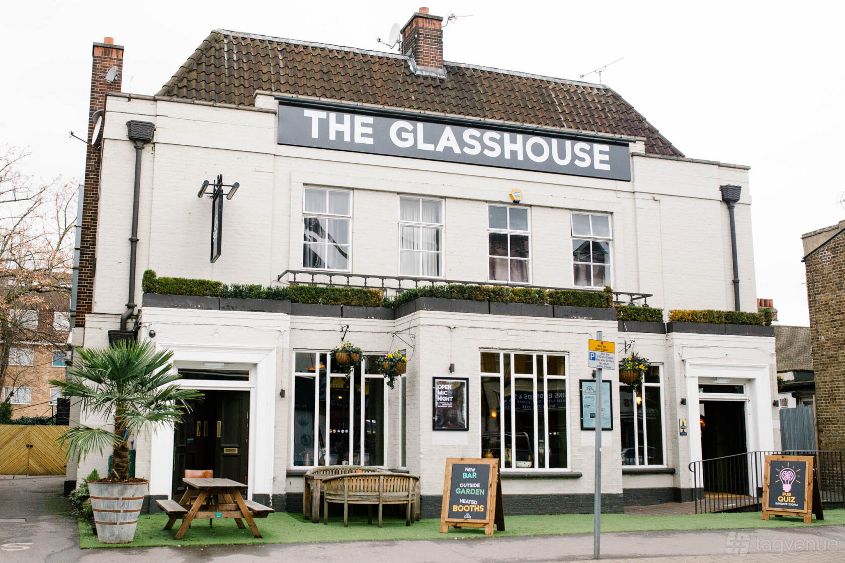 A white-painted pub with large windows, outdoor seating, and hanging planters at The Glasshouse.