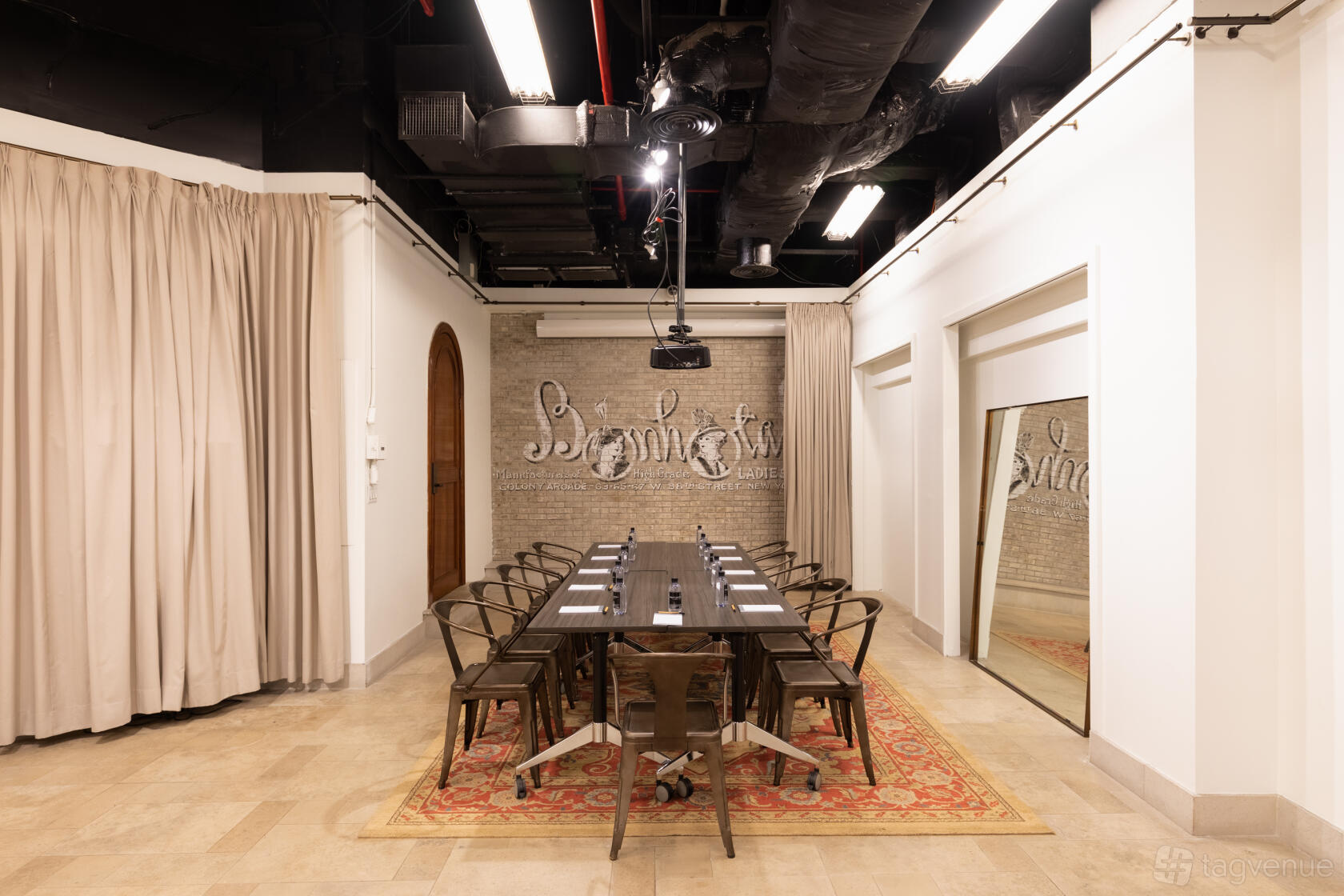 An event venue with exposed brick walls, a long meeting table, industrial chairs, and a ceiling projector at Hatbox Flex Space.