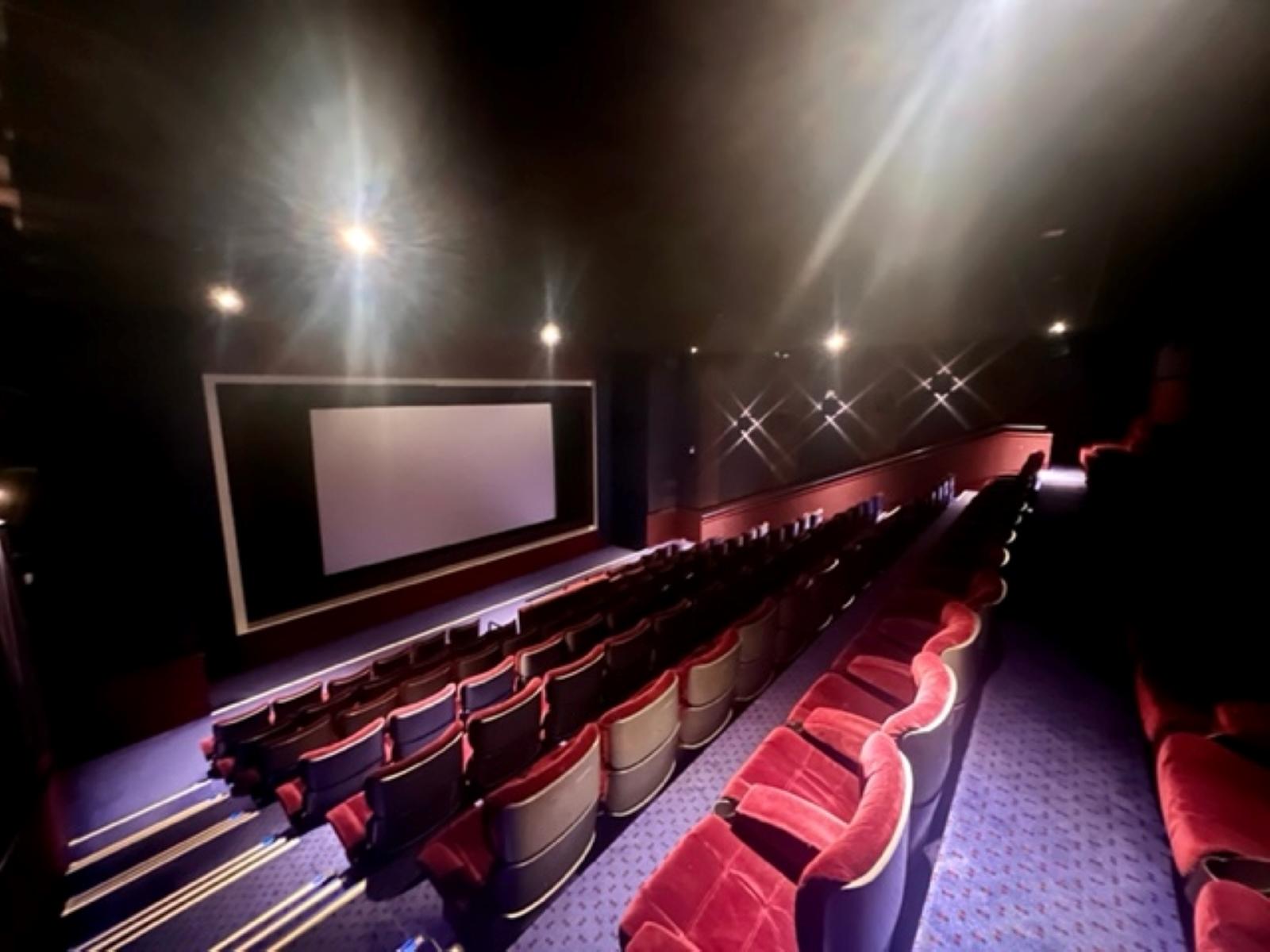 A cinema with red velvet seats, a large screen, and dark walls with aisle lighting at Vue Piccadilly.