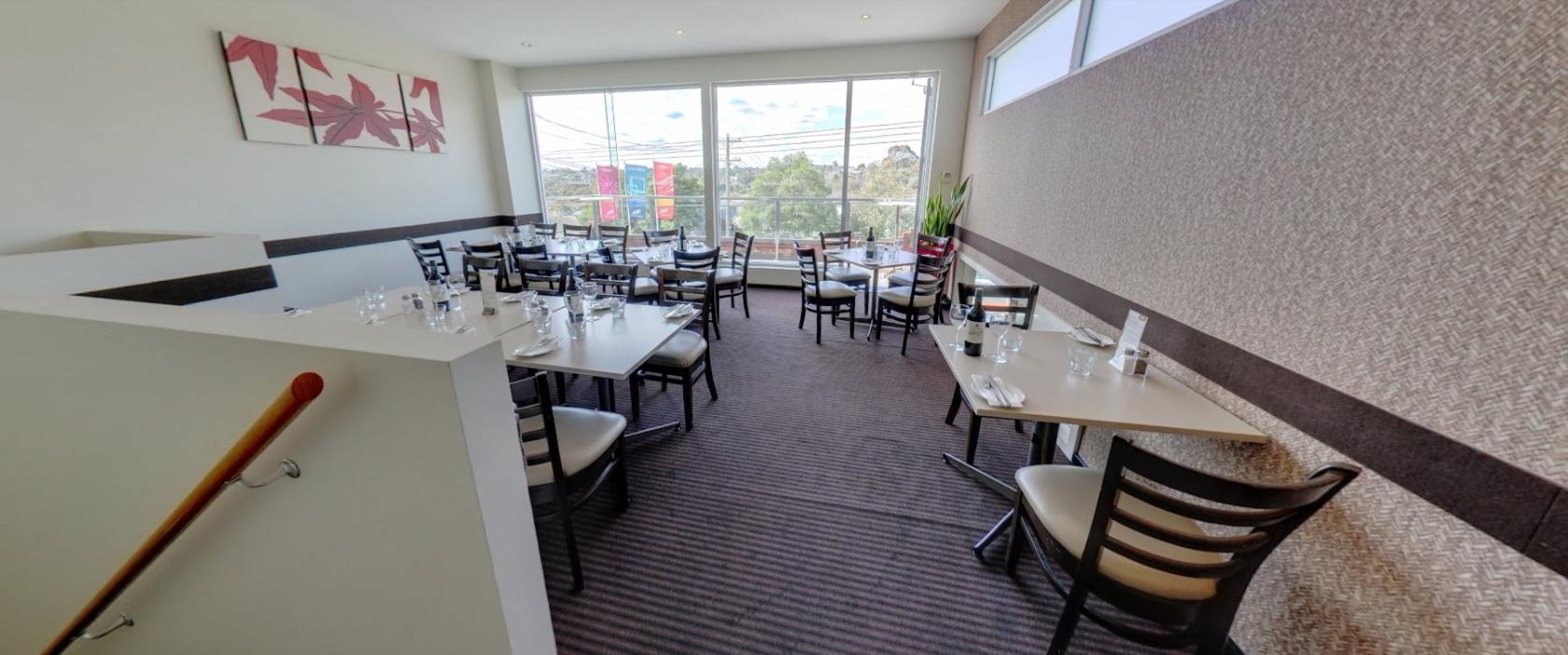 A restaurant dining area with large windows, natural light, and set tables at Vibrante Restaurant.