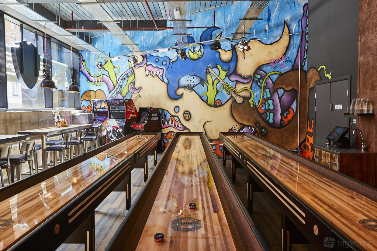 A bar with shuffleboard tables, arcade games, and a colorful mural wall at BrewDog Outpost Tower Hill.