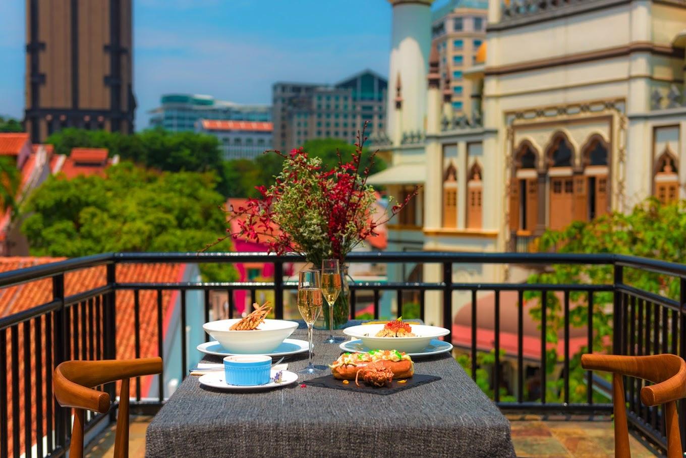 A terrace dining area with a table set for two, floral centerpiece, and city views at Maison Ikkoku.