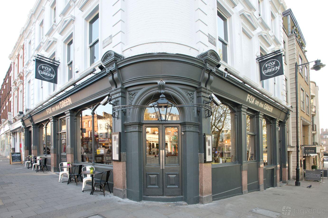 A street corner pub with large windows, black trim, and outdoor seating at Fox On The Green.