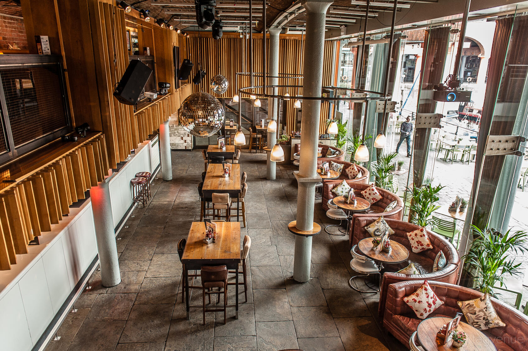 A bar in a restaurant with floor-to-ceiling windows, high tables, and leather sofas at Revolution Liverpool Albert Dock.