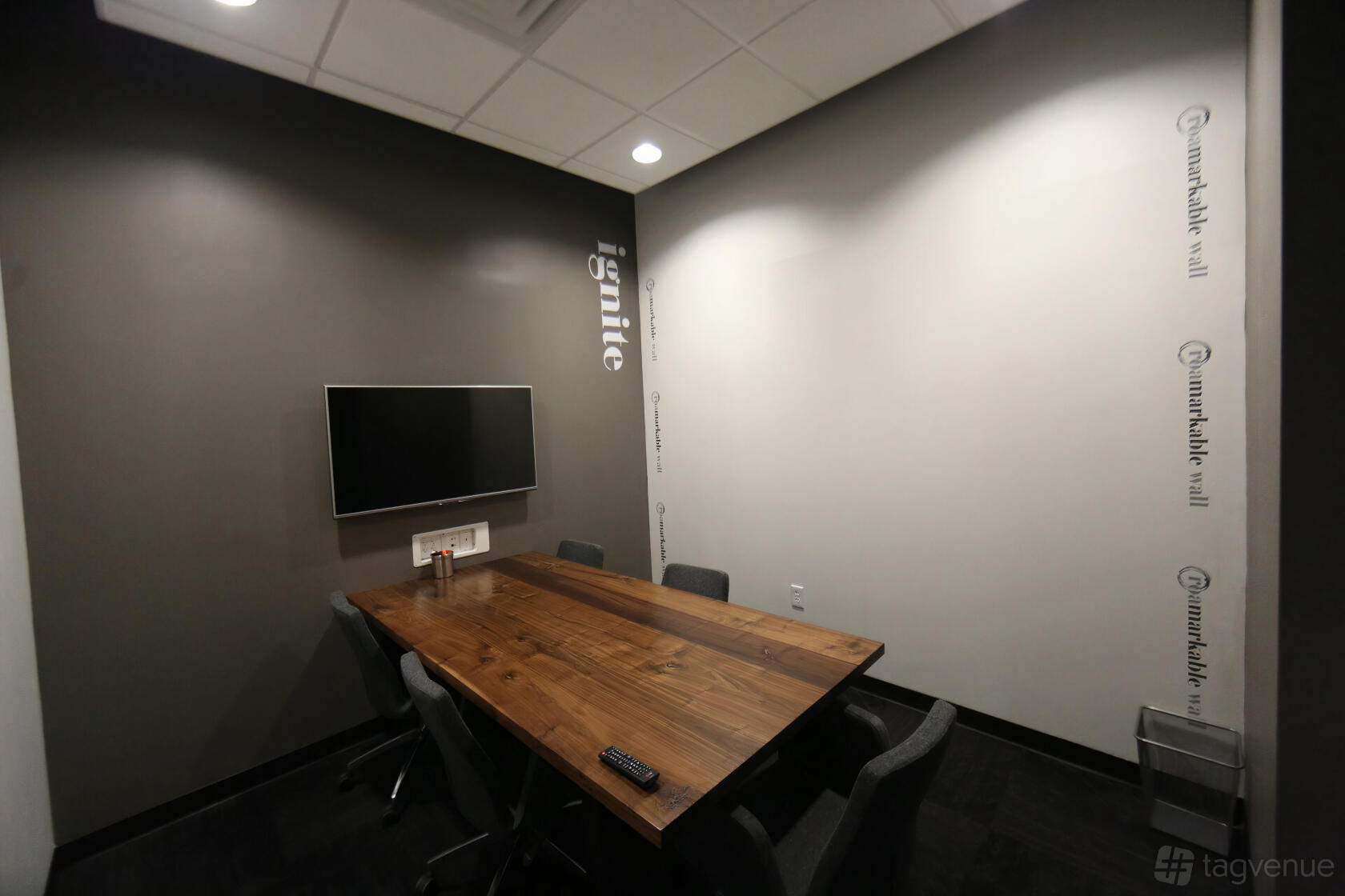 A meeting room with a wooden conference table, wall-mounted TV, and minimalist decor at ROAM GALLERIA.