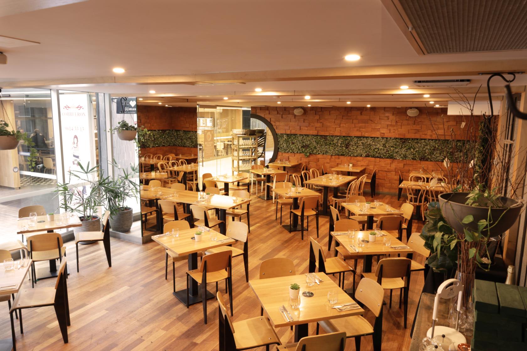 A function room in a restaurant with wooden tables, modern chairs, potted plants, and a feature greenery wall at Henry & the Fox.