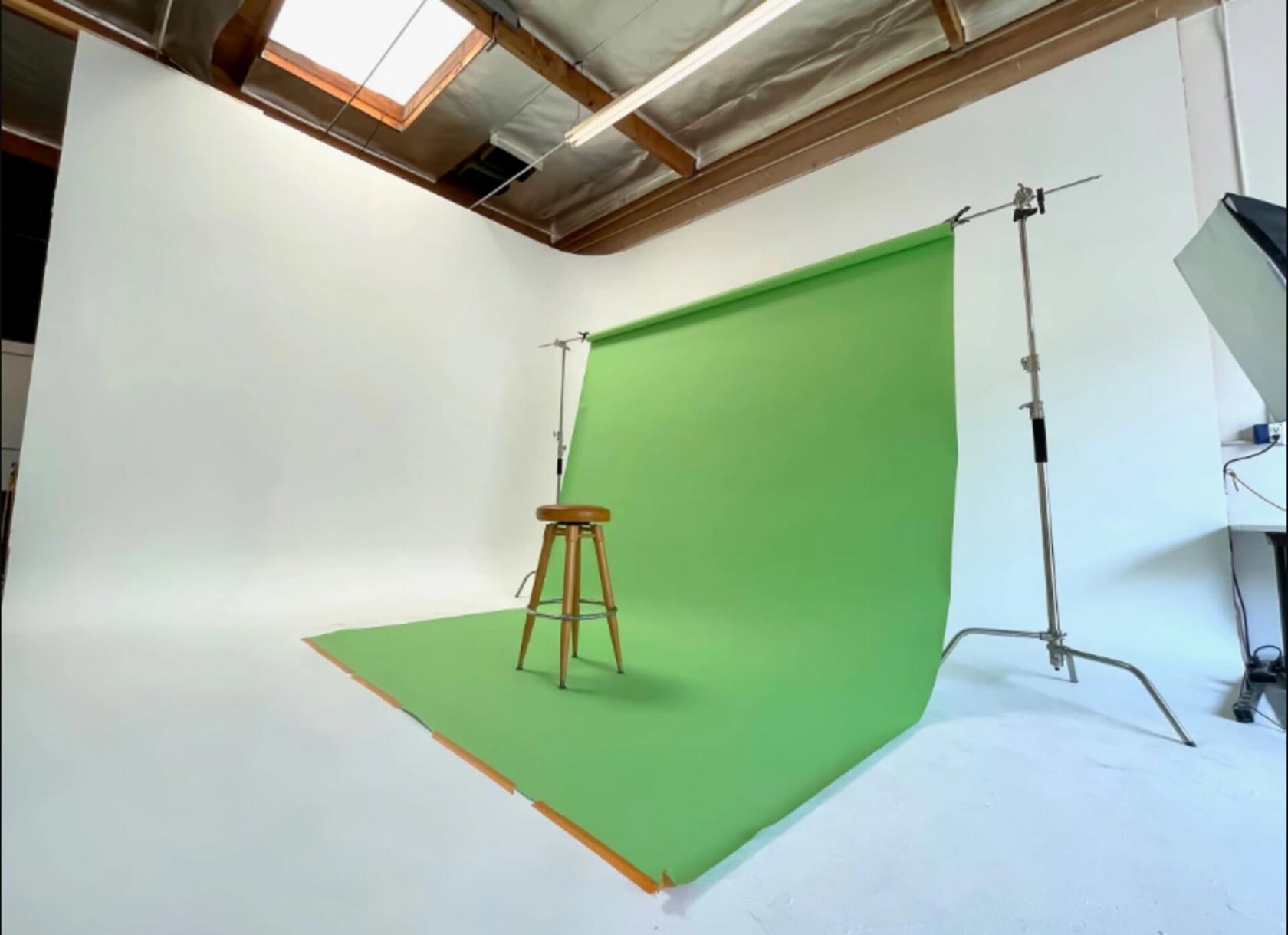 A photo studio with a green screen backdrop, wooden stool, and high ceilings with exposed beams at Orange County Photo.