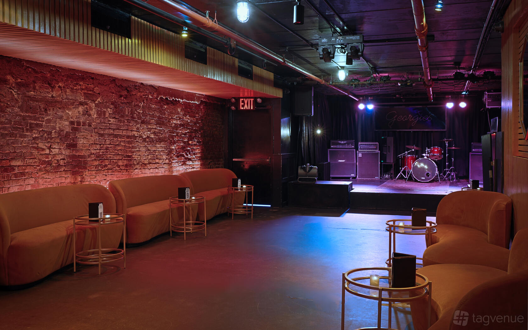 A nightclub basement with exposed brick walls, stage setup, neon lighting, and plush lounge seating at The Delancey.