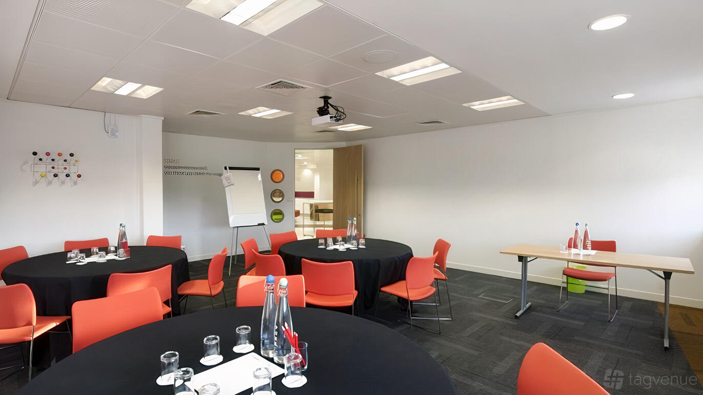 A conference centre with round tables, orange chairs, and presentation equipment at The Studio Glasgow.