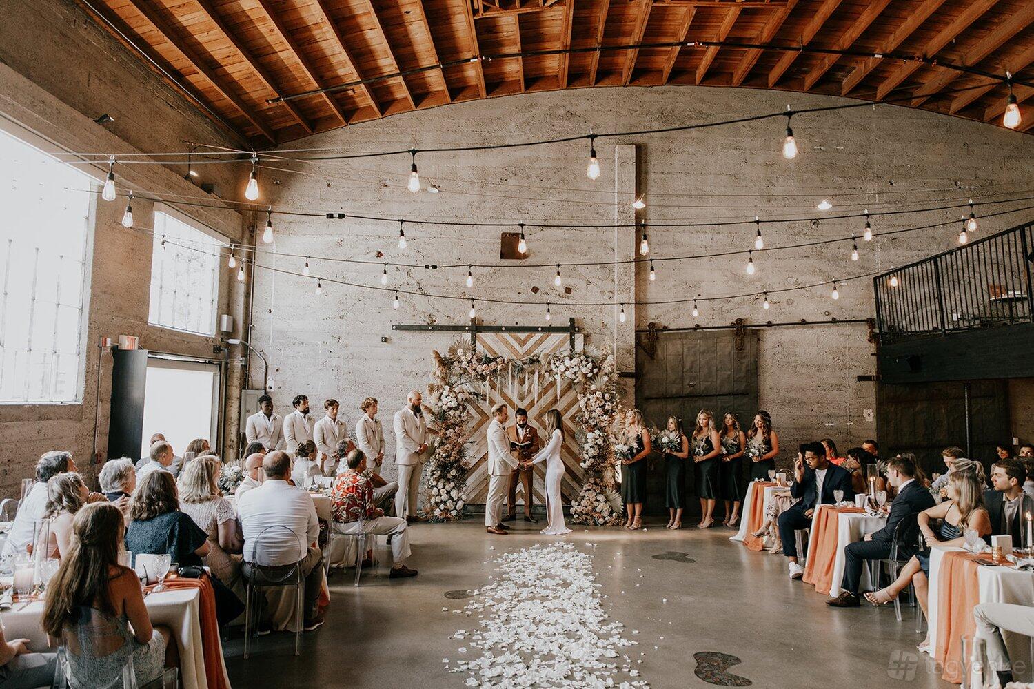 A loft with exposed wood ceilings, string lights, and a decorative floral ceremony arch at Luce Loft.