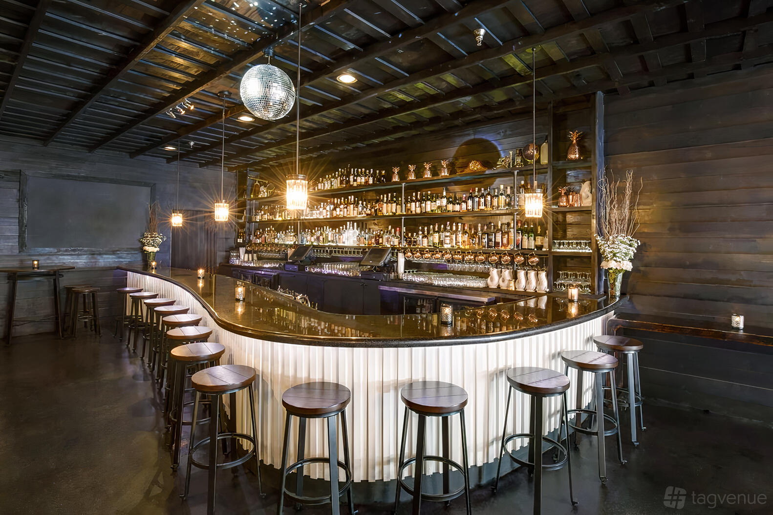 A bar with a curved counter, high stools, backlit shelving, and a disco ball at The Eleanor.