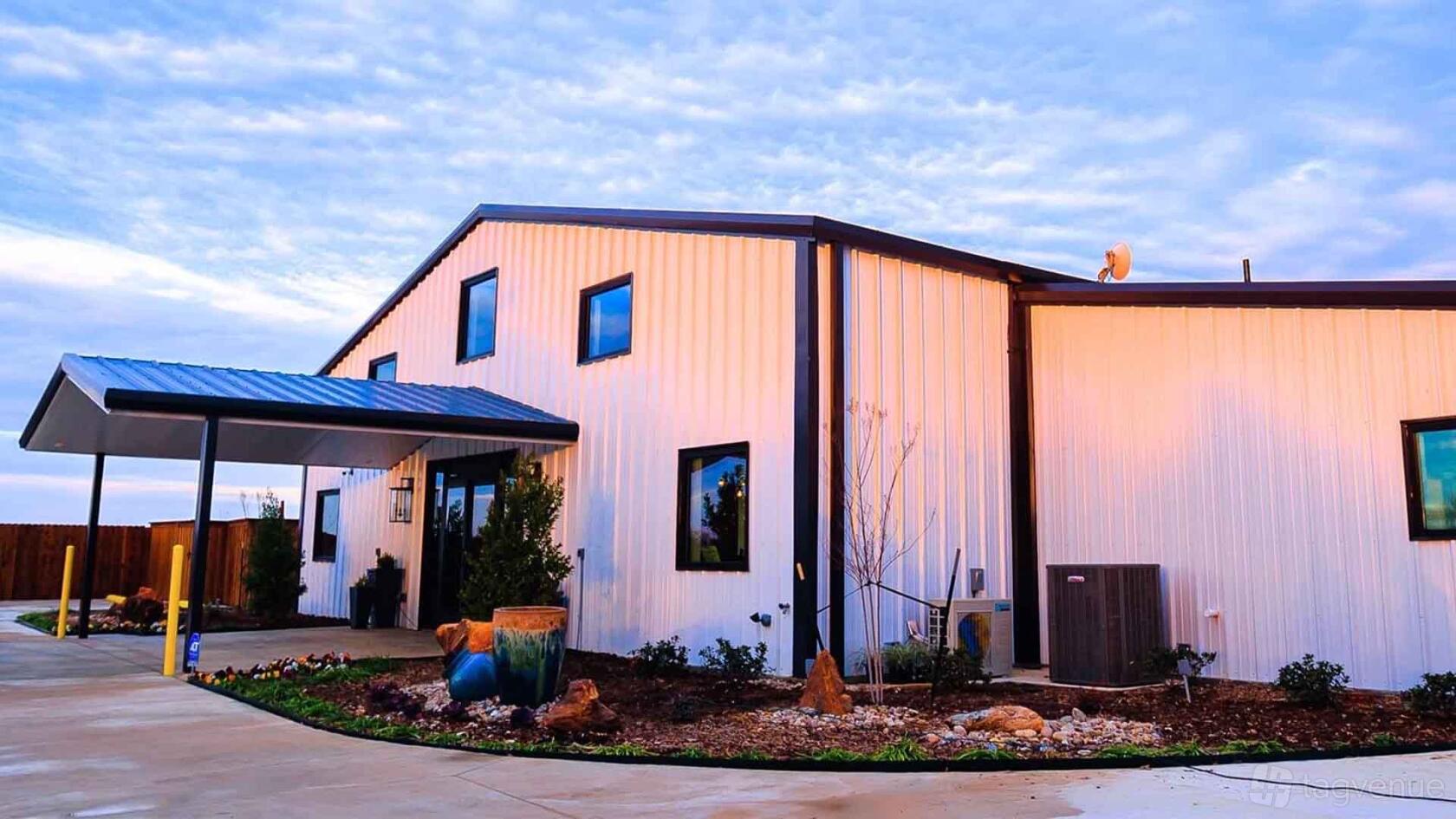 A country house with white metal siding, black-framed windows, and landscaped entry at The Acre At 920.