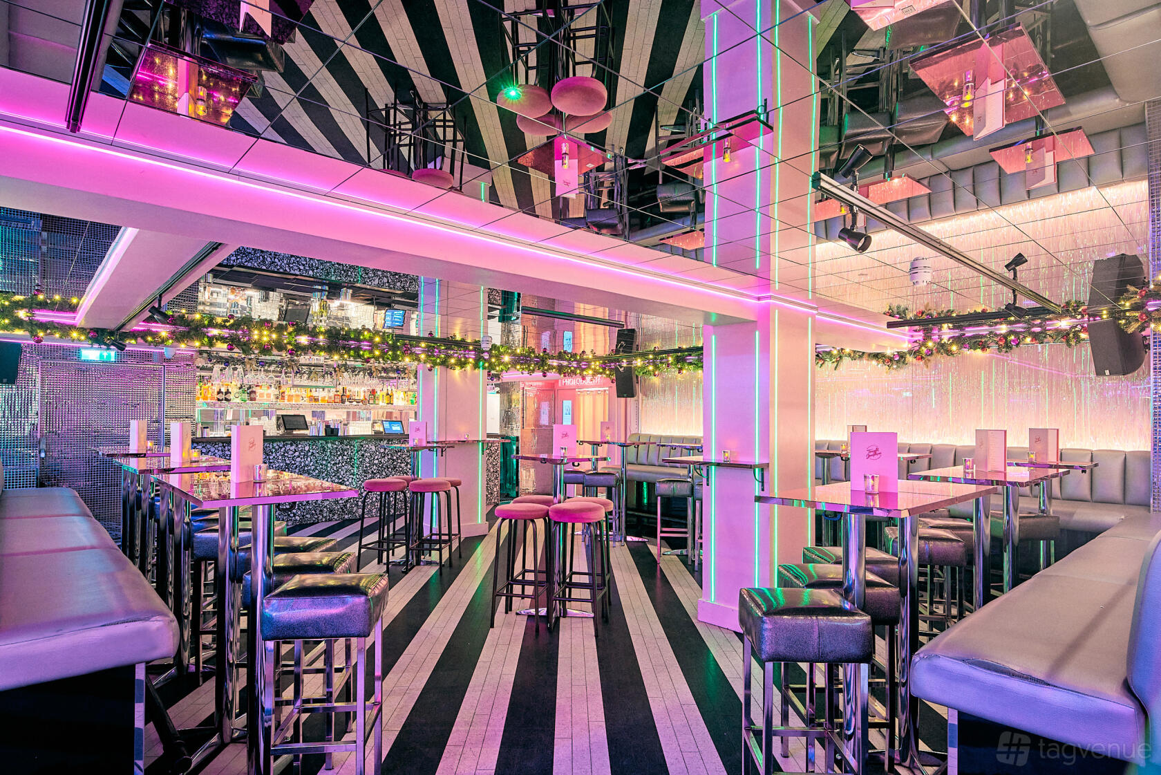 An event space with pink neon lighting, mirrored ceilings, and high tables with bar stools at Tonight Josephine Waterloo.