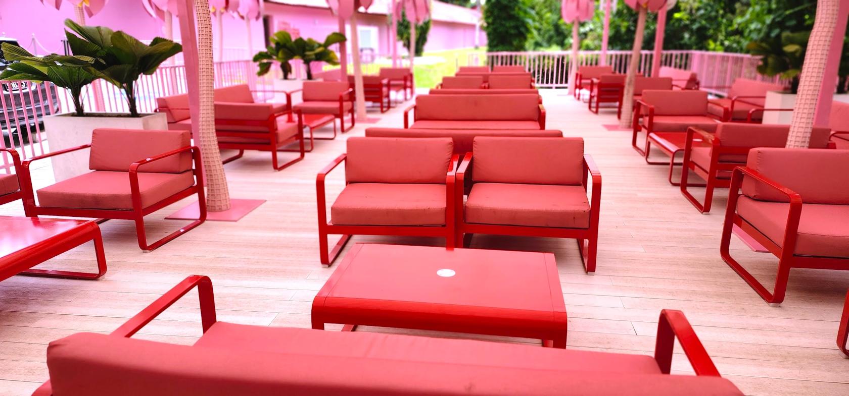 An outdoor cafe with pink and red lounge seating, palm-shaped umbrellas, and light wooden decking at Museum of Ice Cream.