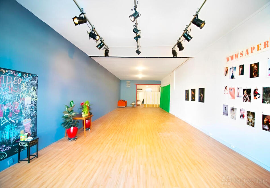 A theatre with wood flooring, blue accent wall, wall art, and overhead stage lighting at All Out Comedy Theater.