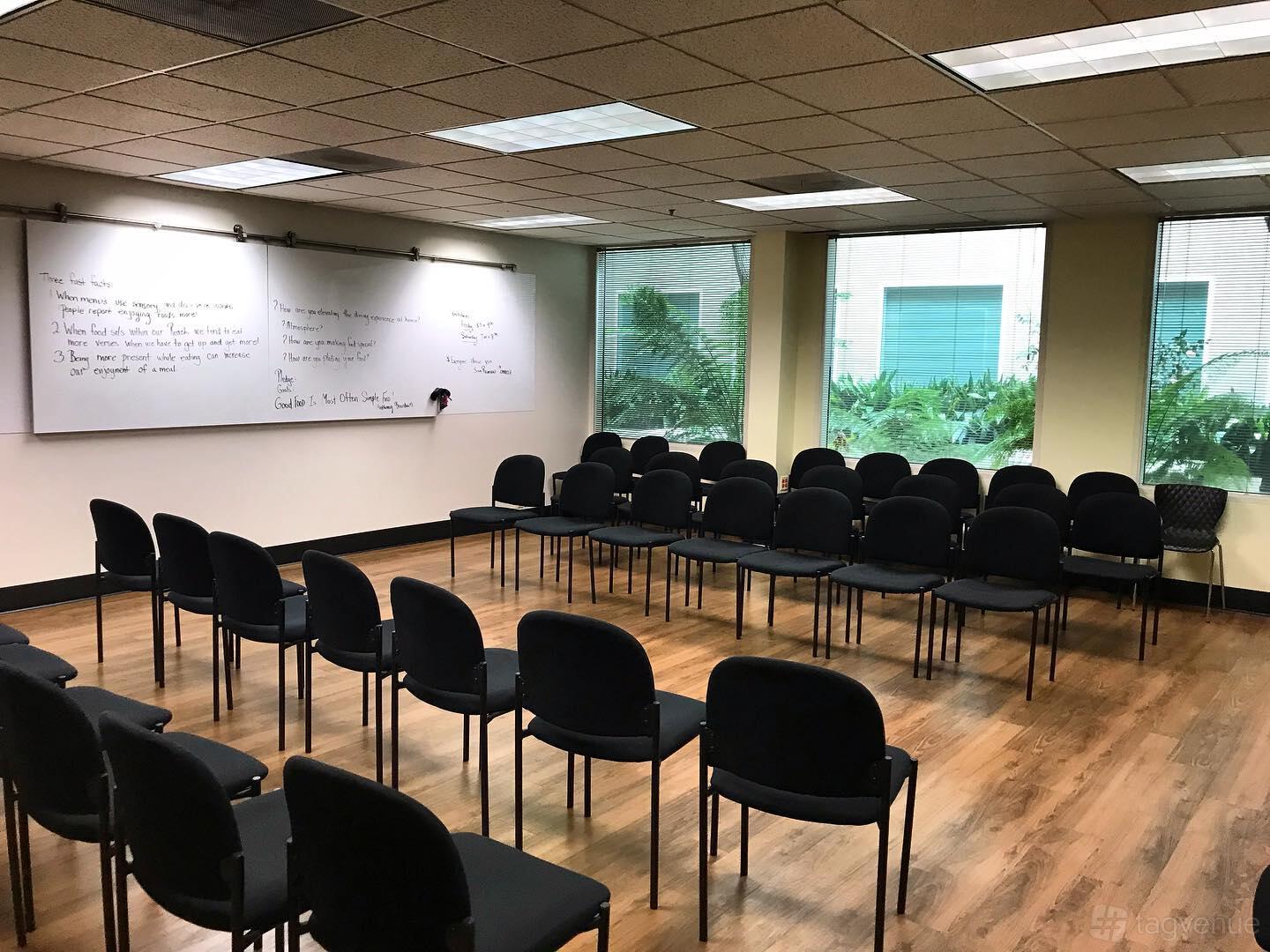 A conference room with rows of black chairs, large windows, and two whiteboards at One Eleven One Ninety.