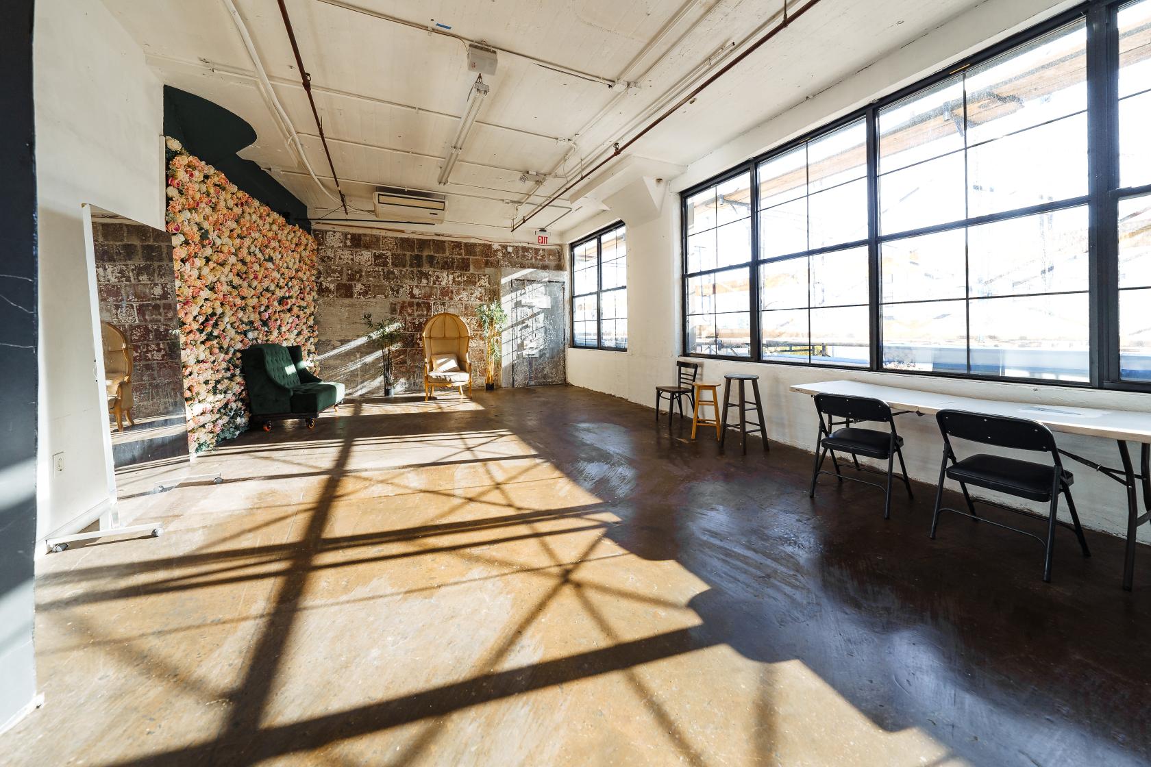A photo studio with large industrial windows, polished concrete floors, and a floral accent wall at N.Y. Studios.
