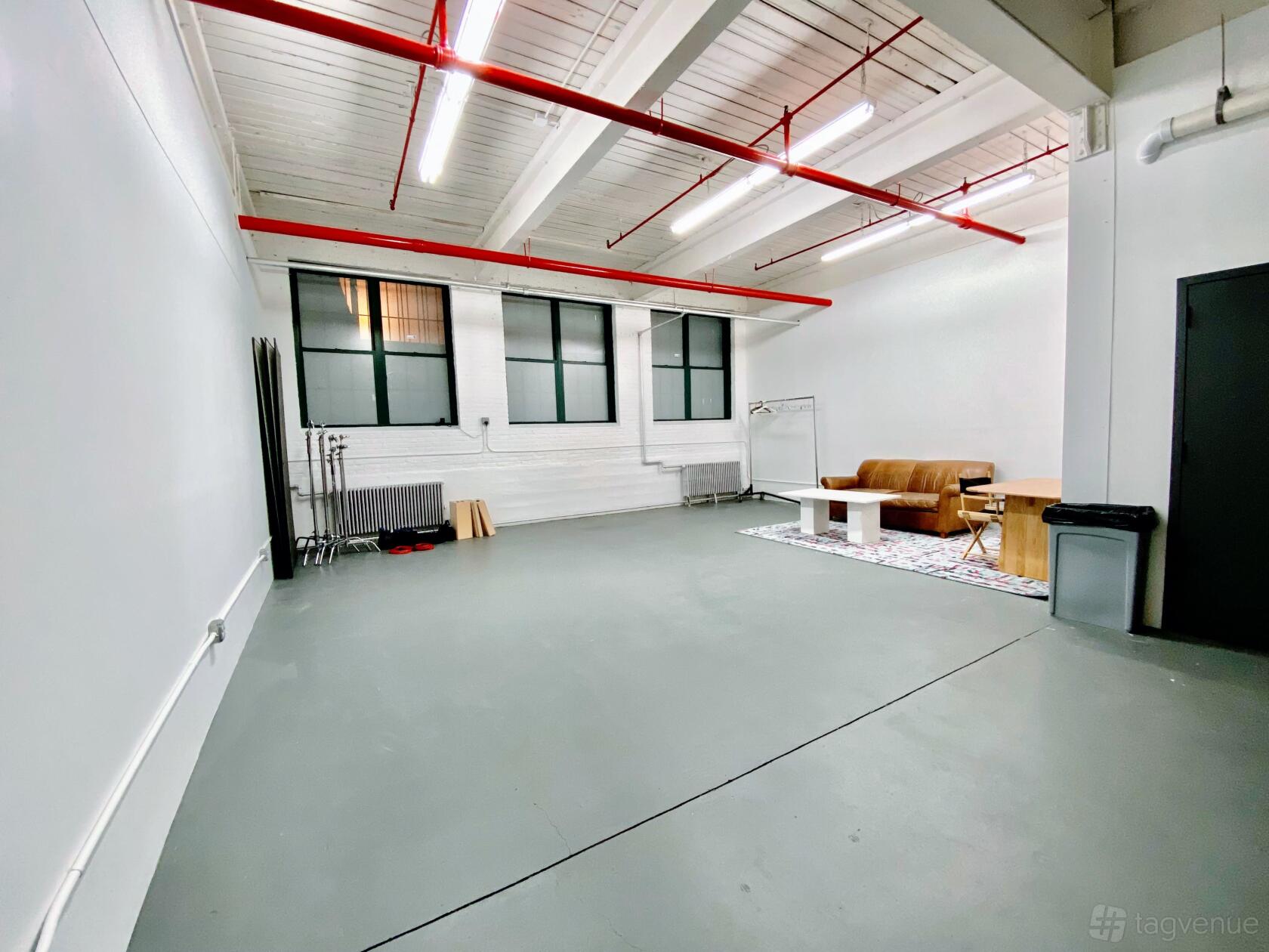A photo studio with white walls, gray flooring, large windows, and a seating area with a sofa at Dangerworks Studio 004.