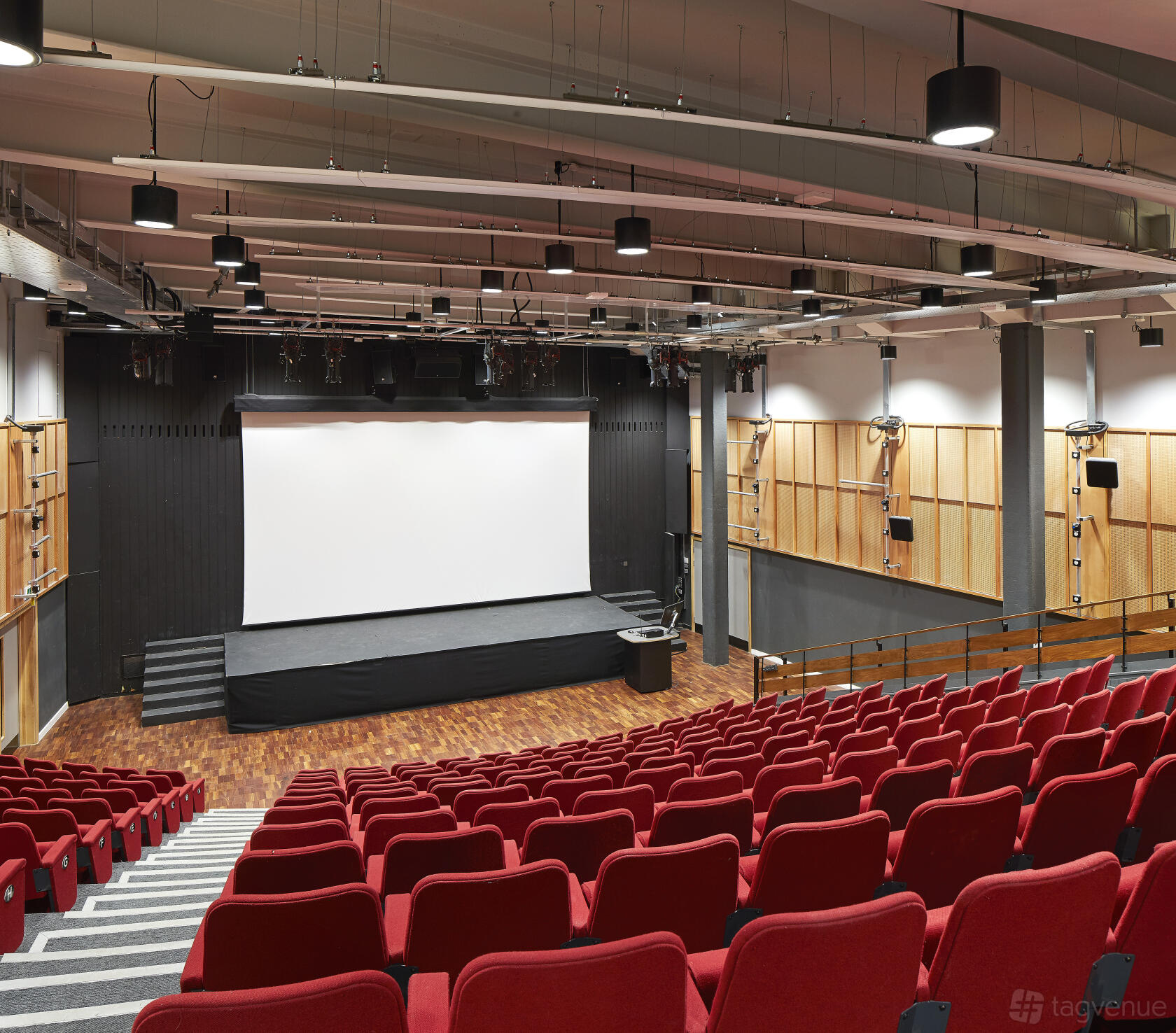 A university theatre with red tiered seating, a large projection screen, and wood-paneled walls at University of Bristol Students' Union.