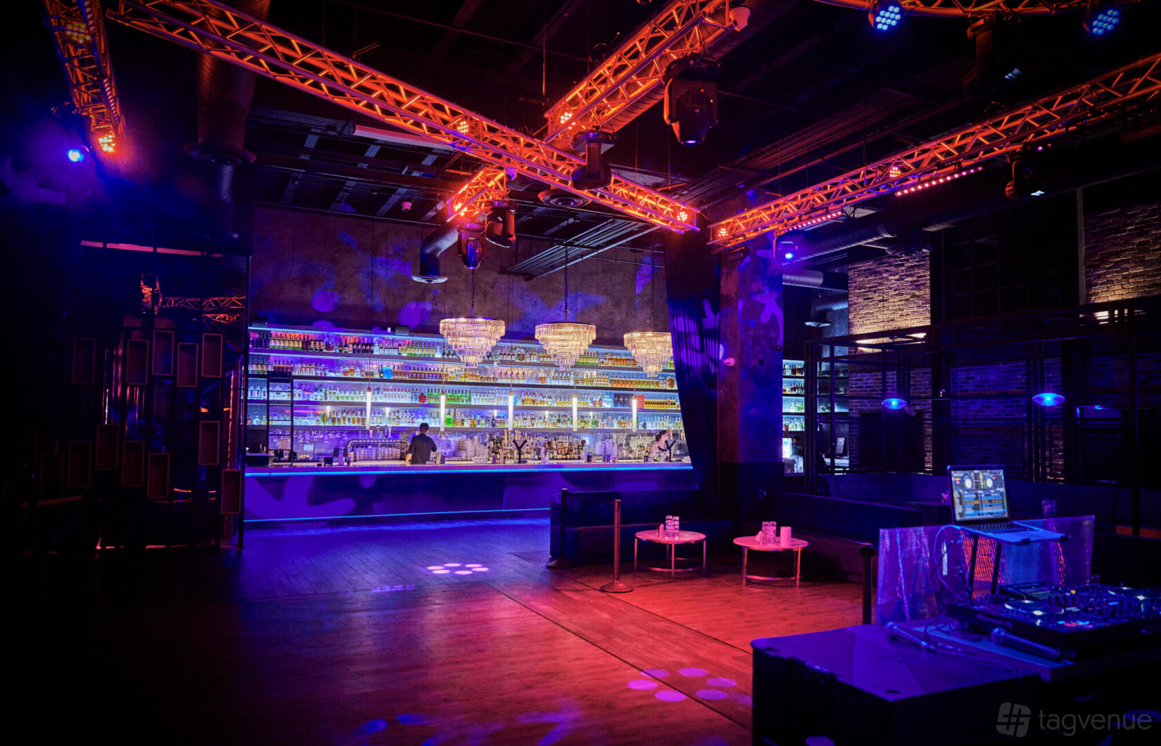 A nightclub bar with a backlit liquor display, chandeliers, DJ booth, and spacious dance floor at Terracotta.
