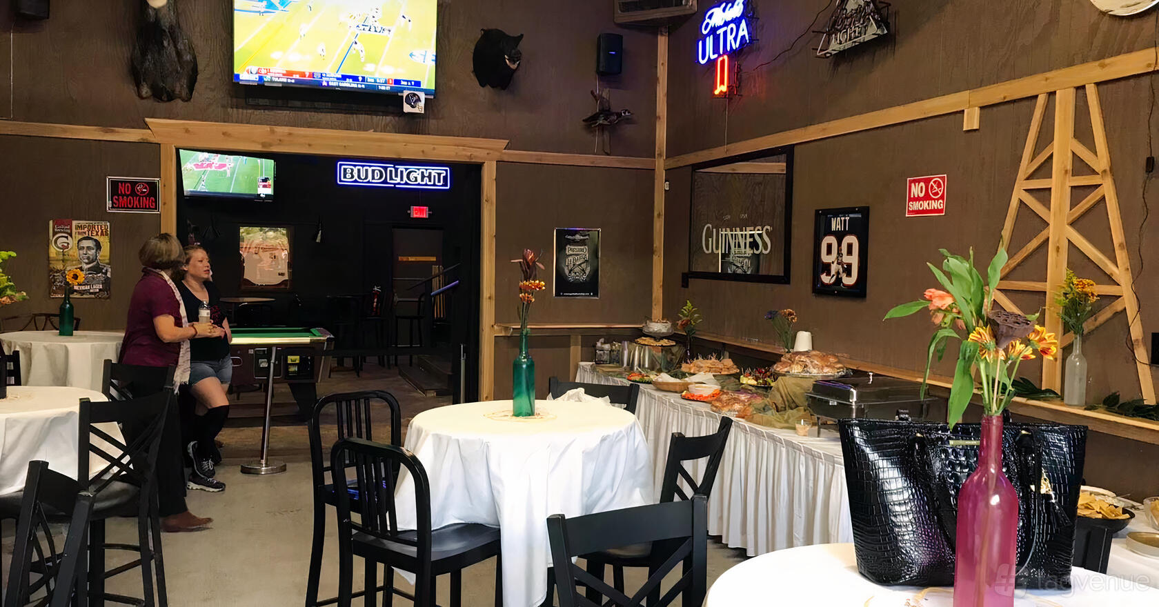 A bar with round tables, black chairs, wall-mounted TVs, neon signs, and a buffet setup at Texas T. Tavern.