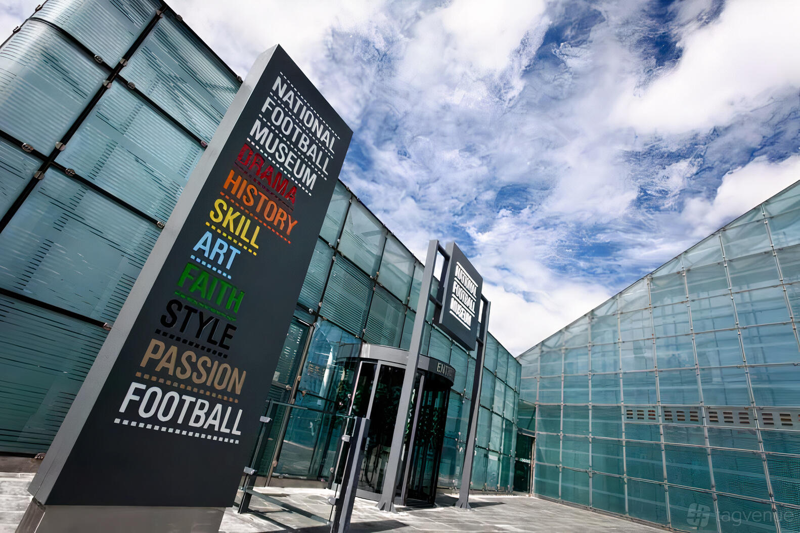 A museum entrance with glass facades and a tall sign listing themes at the National Football Museum.