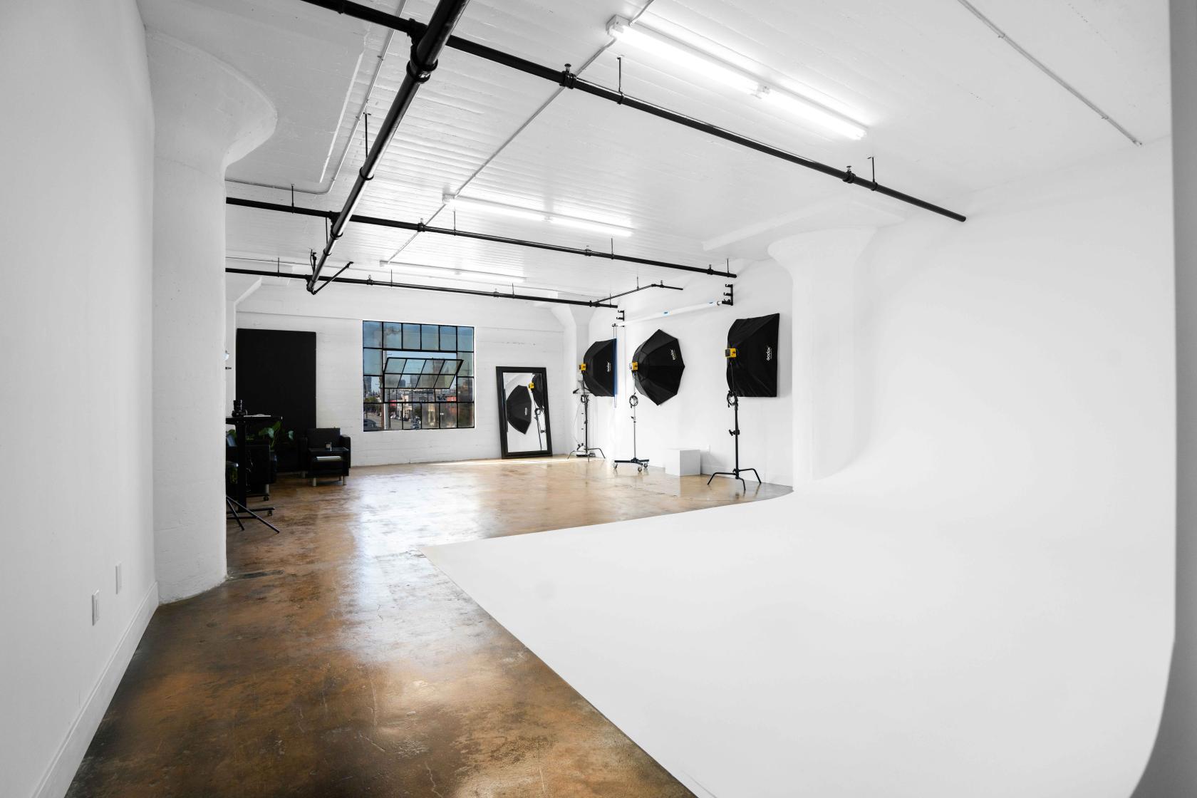 A photo studio with white cyclorama walls, polished concrete floor, and studio lights at MNML Photo Studio.