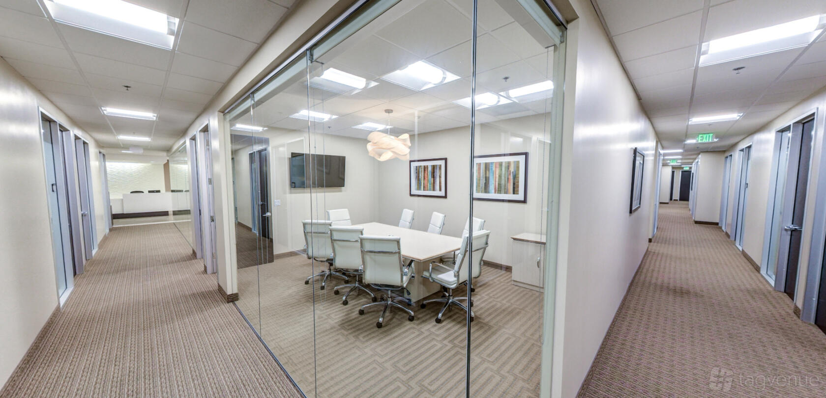 A glass-enclosed meeting room with a long white table, white office chairs, and wall art at Premier Workspaces - Del Mar Corporate Plaza.