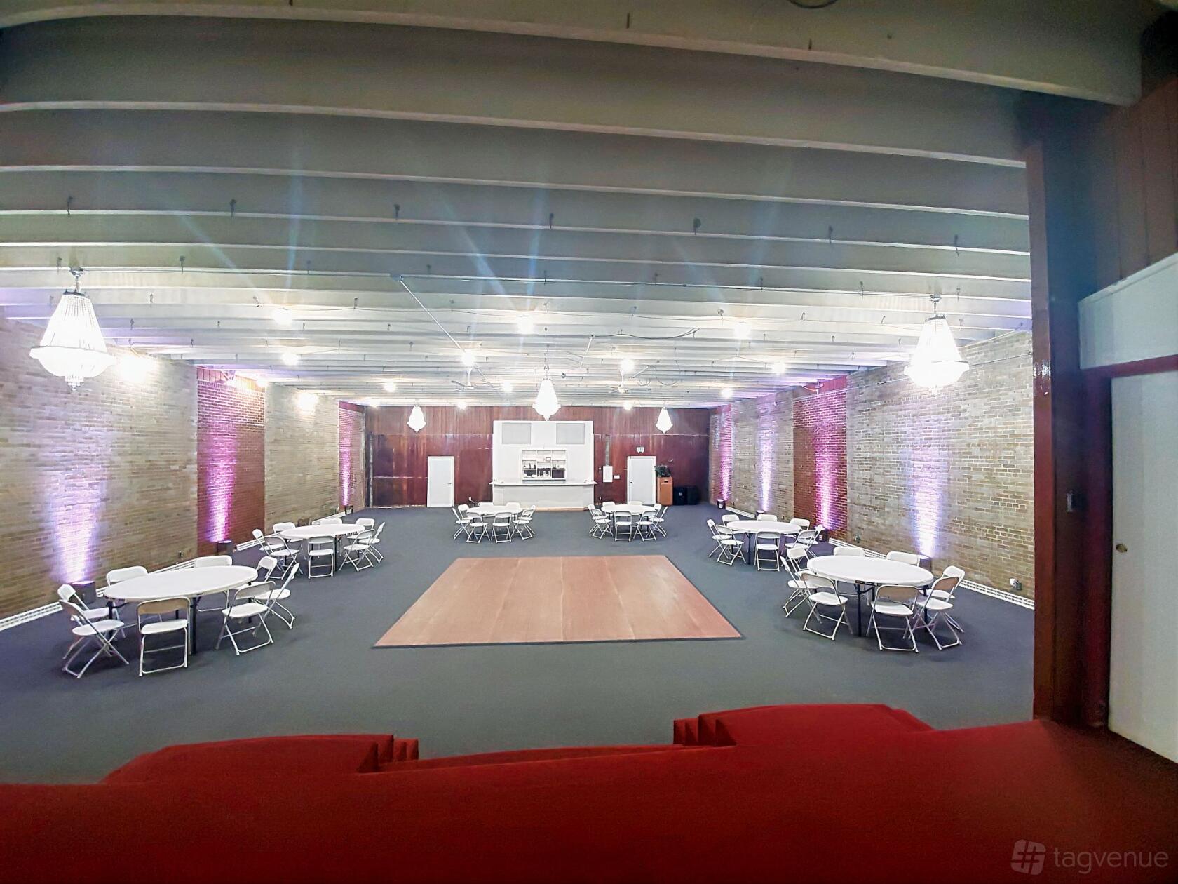 An event venue with exposed beam ceiling, brick walls, round tables with chairs, and chandeliers at MM&E Banquets & Events.