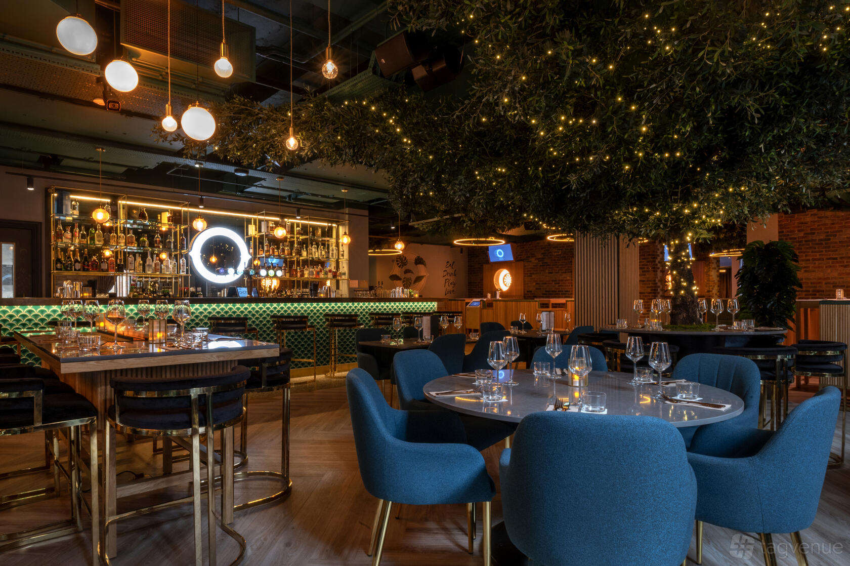 An event venue in a bar with velvet blue chairs, round tables set with glassware, and a backlit bar at Oche.