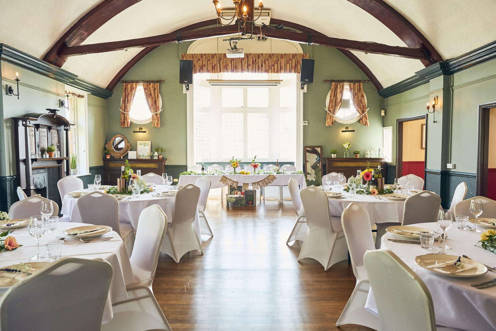 An event space in a pub with round tables draped in white linens, wooden floors, and exposed ceiling beams at The Royal Oak.