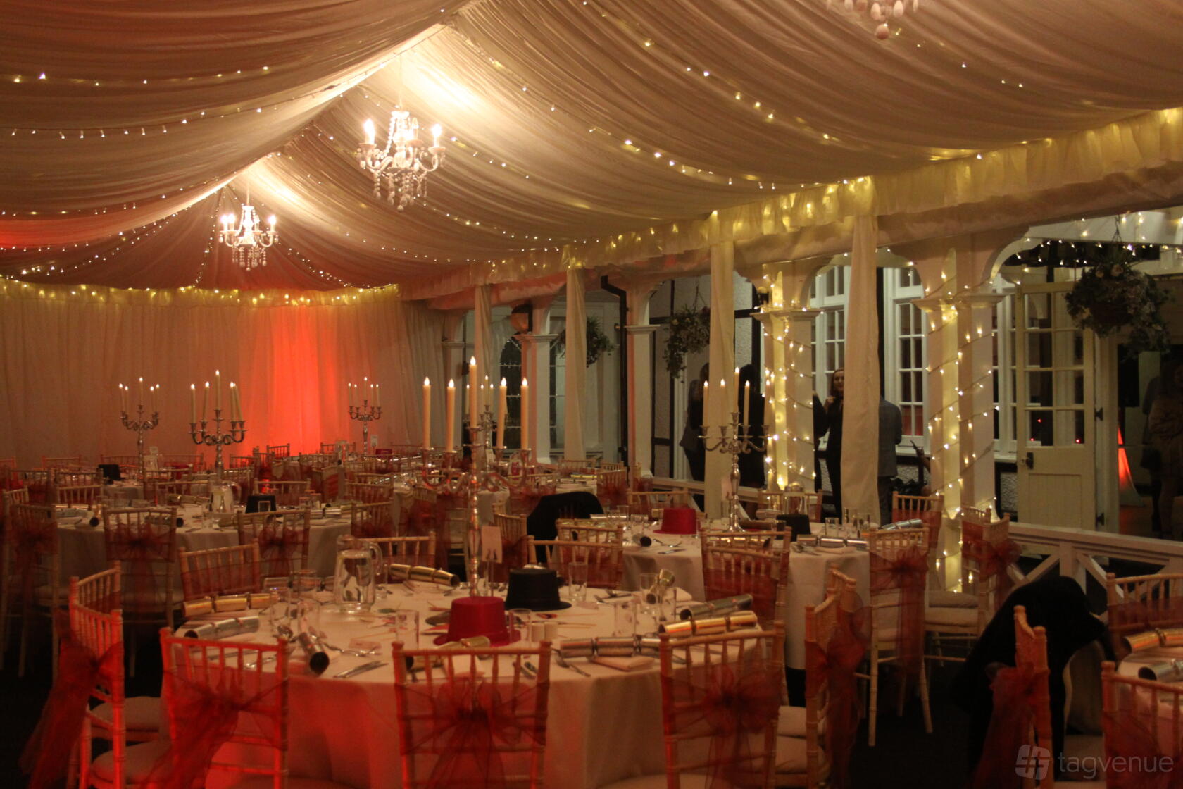 A hall with draped ceilings, chandeliers, fairy lights, and round tables with white linens at London Shenley Club.