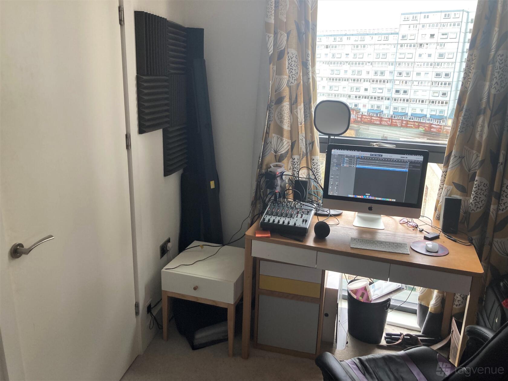 A podcast studio with a desktop computer, audio mixer, foam soundproof panels, and natural light at Chazz Redhead Studios.
