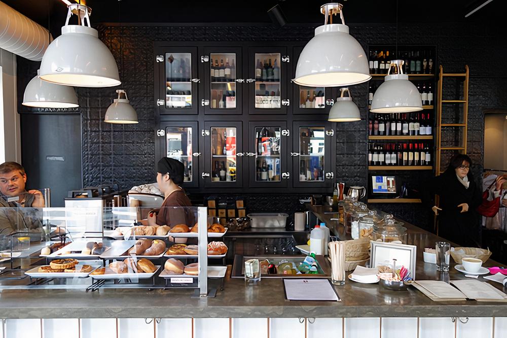 A restaurant with a pastry display counter, pendant lights, and wall shelves stocked with wine at Tarallucci e Vino Upper West Side.