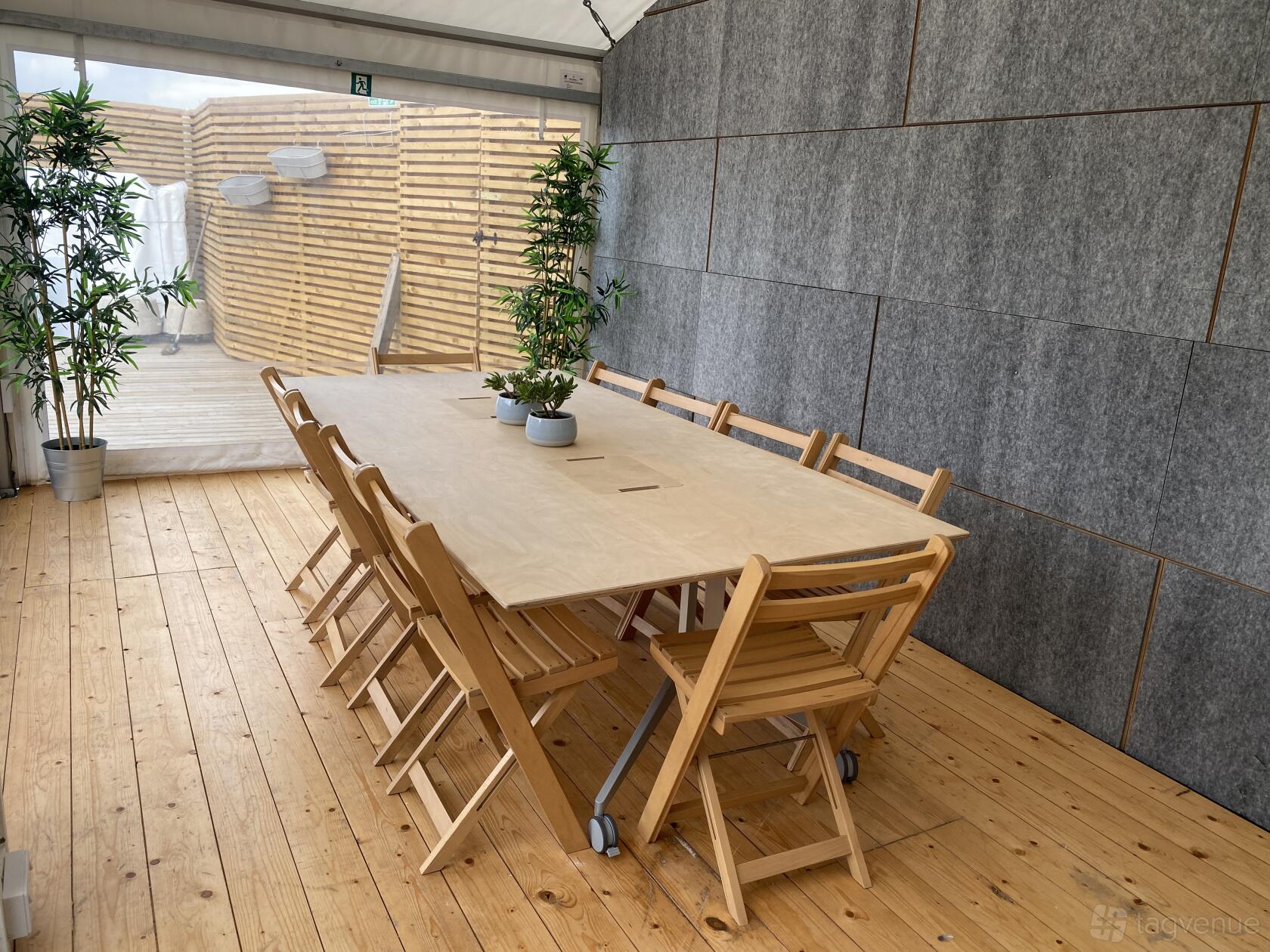 A meeting room with a large wooden table, folding chairs, potted plants, and wood panel flooring at Bespoke Spaces - Archway.