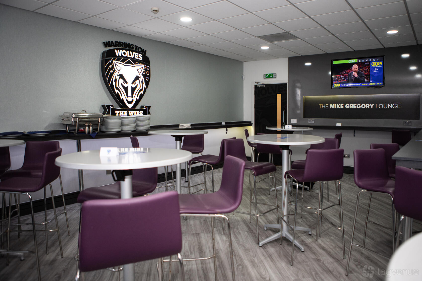 An event space with round tables, purple chairs, and sports-themed decor at The Halliwell Jones Stadium.
