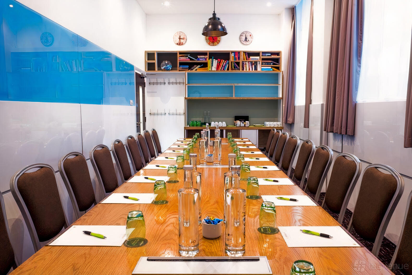 A hotel meeting room with a long wooden table, neatly arranged chairs, notepads, and bookshelves at The Wesley Euston Hotel.