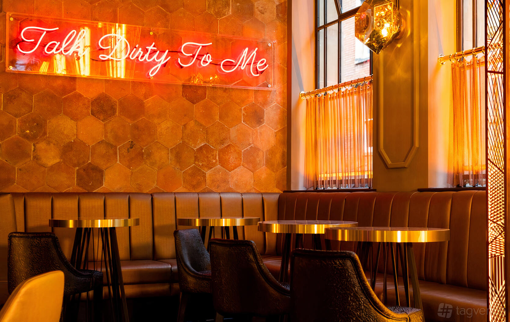 A cocktail bar with gold-accented tables, leather banquette seating, and a neon sign at Dirty Martini Bristol.