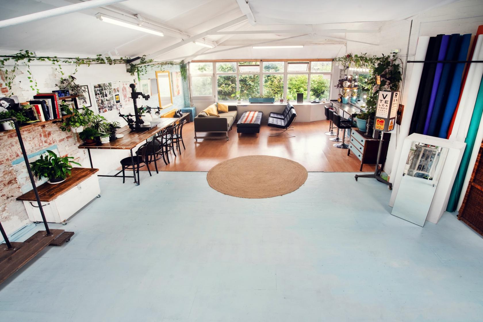 A creative studio with white walls, large windows, plants, lounge seating, and a communal desk at Clerkenwell Studio.