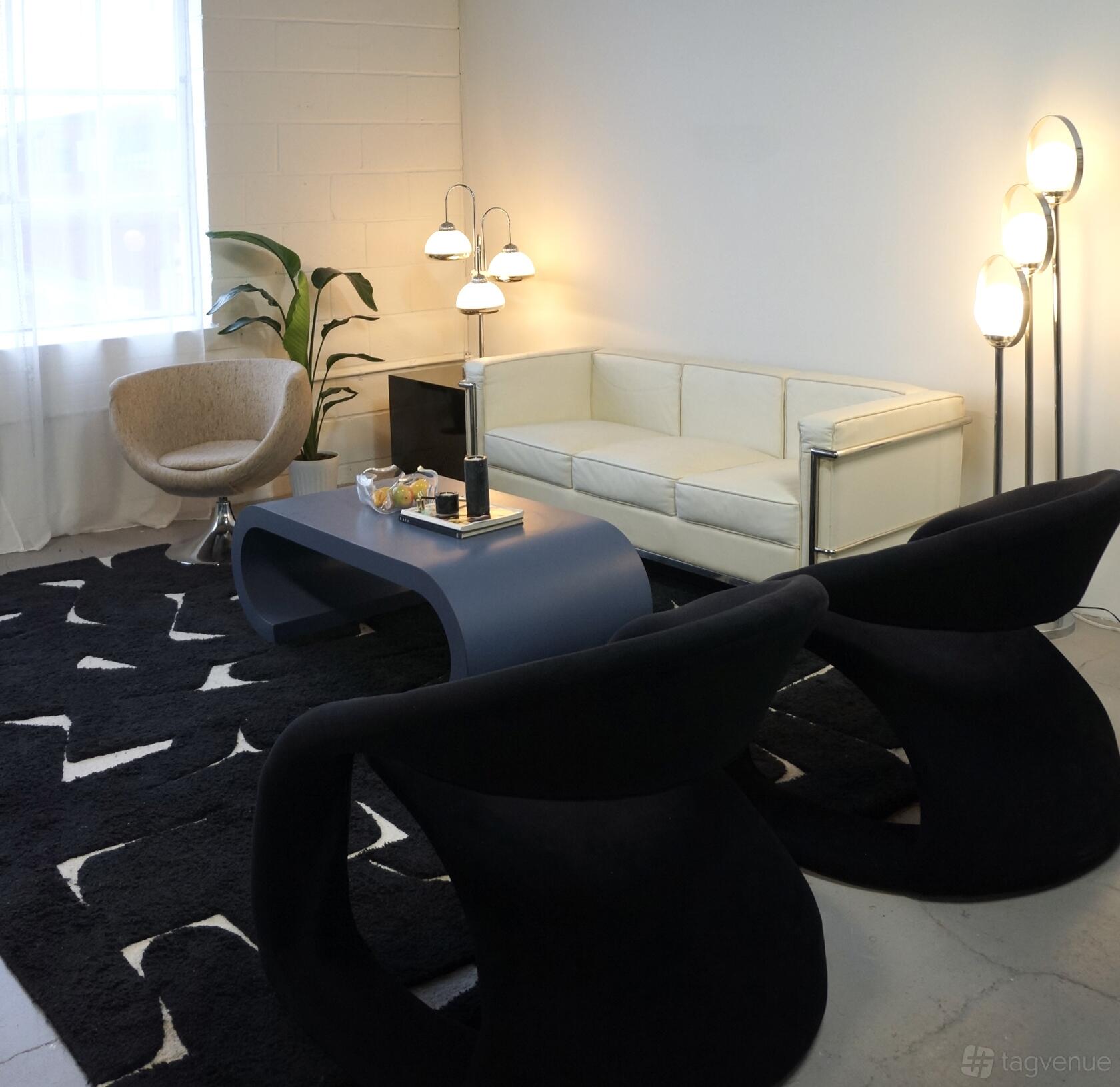 A photo studio with a white couch, modern black chairs, a blue coffee table, and floor lamps at Studio/Era.
