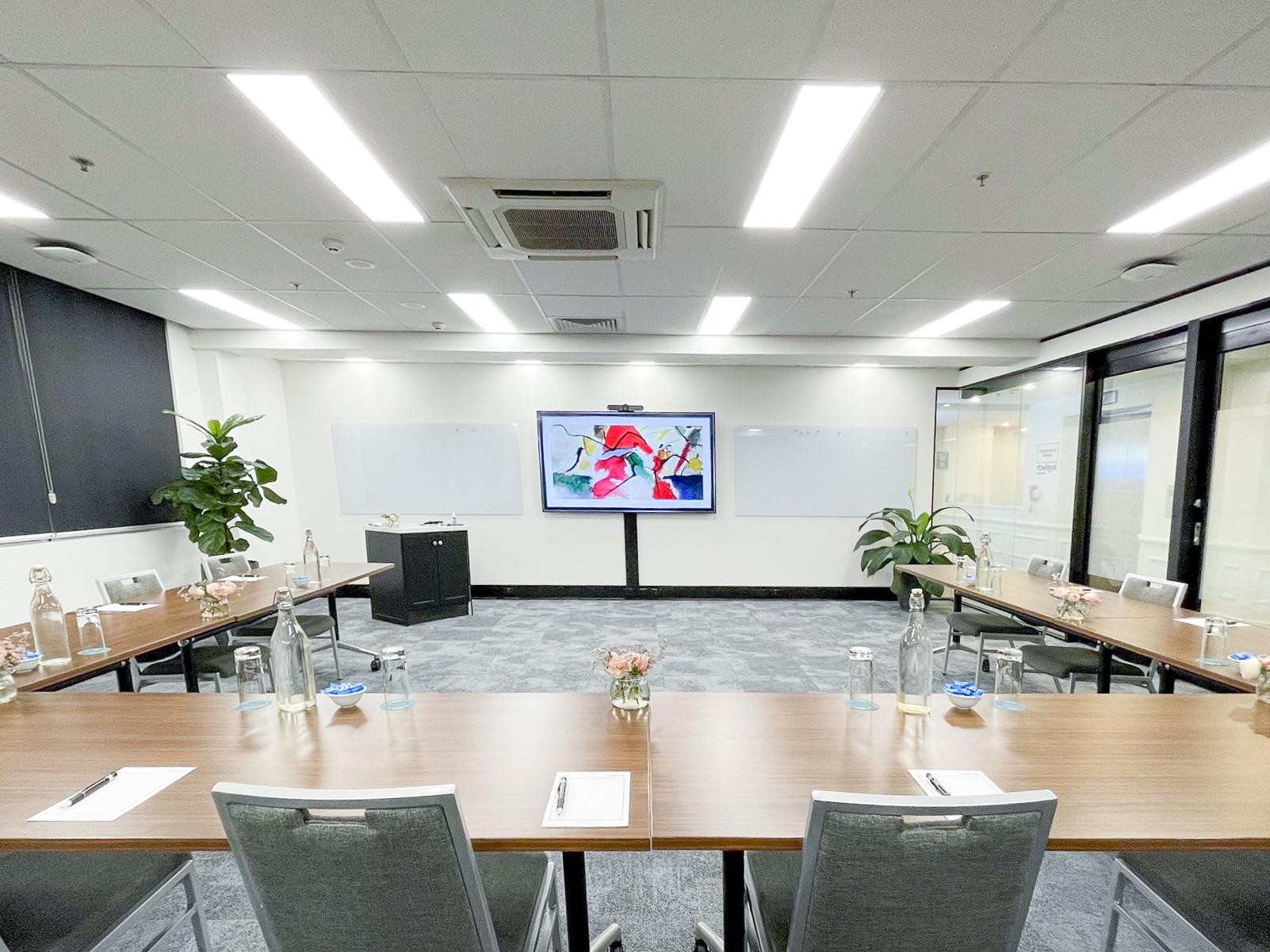 A training room with U-shaped tables, bottled water, notepads, and a large screen at Christie Spaces Conferencing Melbourne.
