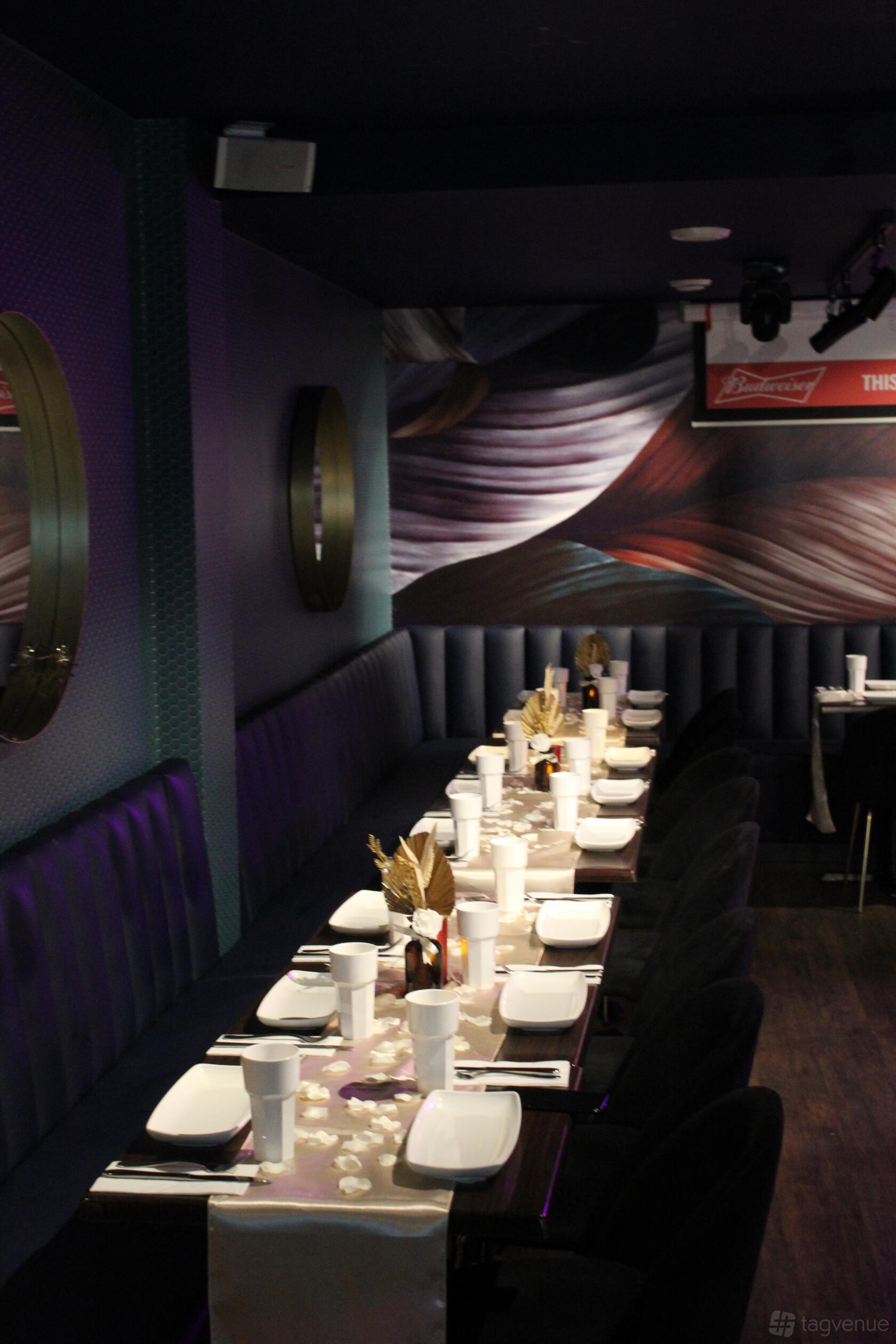 A function room in a restaurant with a long banquet table, plush navy seating, and decorative wall art at Cottons Shoreditch.
