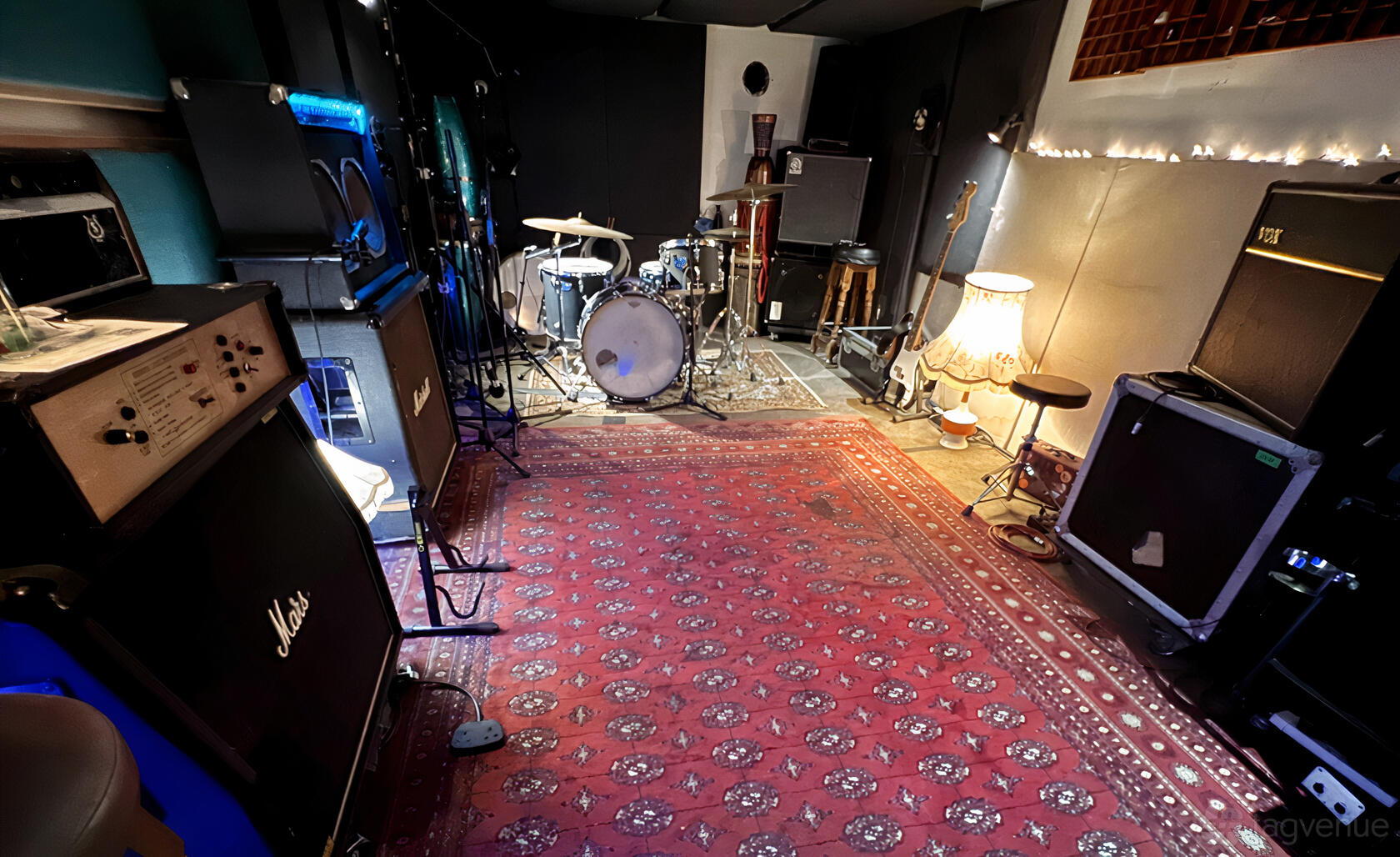 A recording studio with a drum kit, amplifiers, guitars, and a patterned carpet at Hicaz Studio.