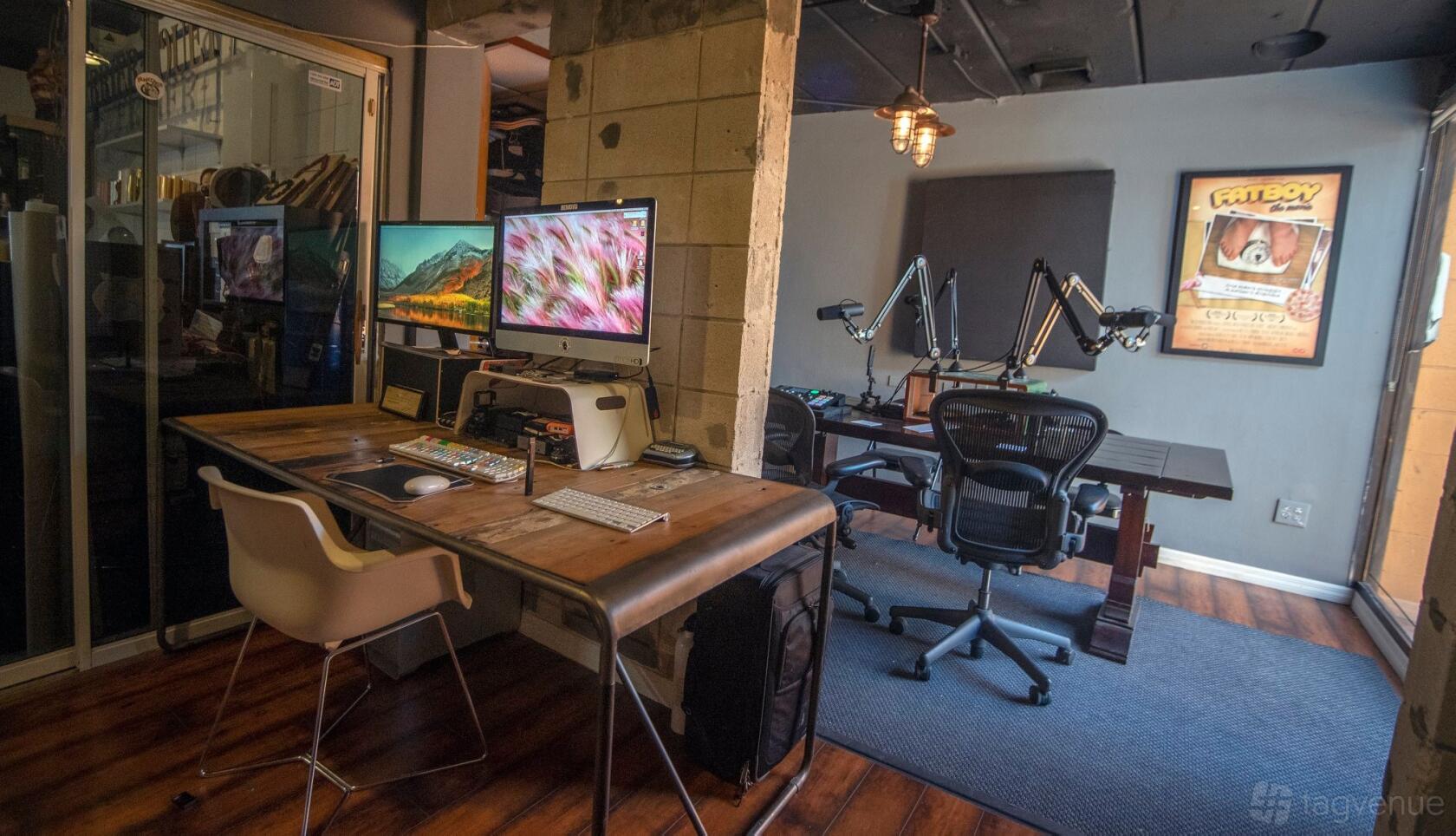 A recording room with a wooden desk, dual monitors, podcast microphones, and soundproofing panels at Unicorn Fire Studios.